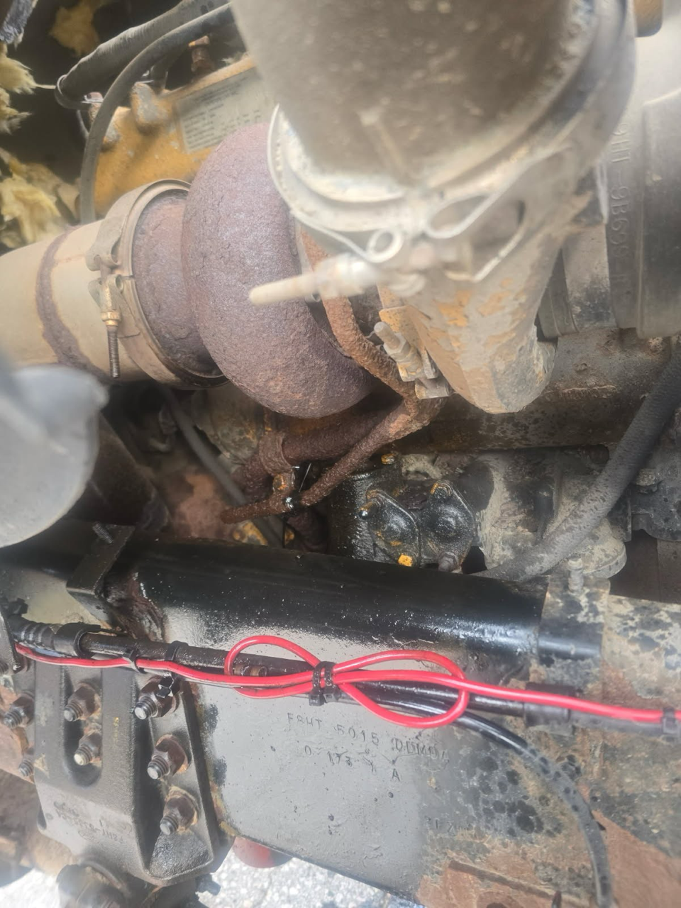 Close-up view of an old, rusty engine with various metal parts, wiring, and a black metal support beam.