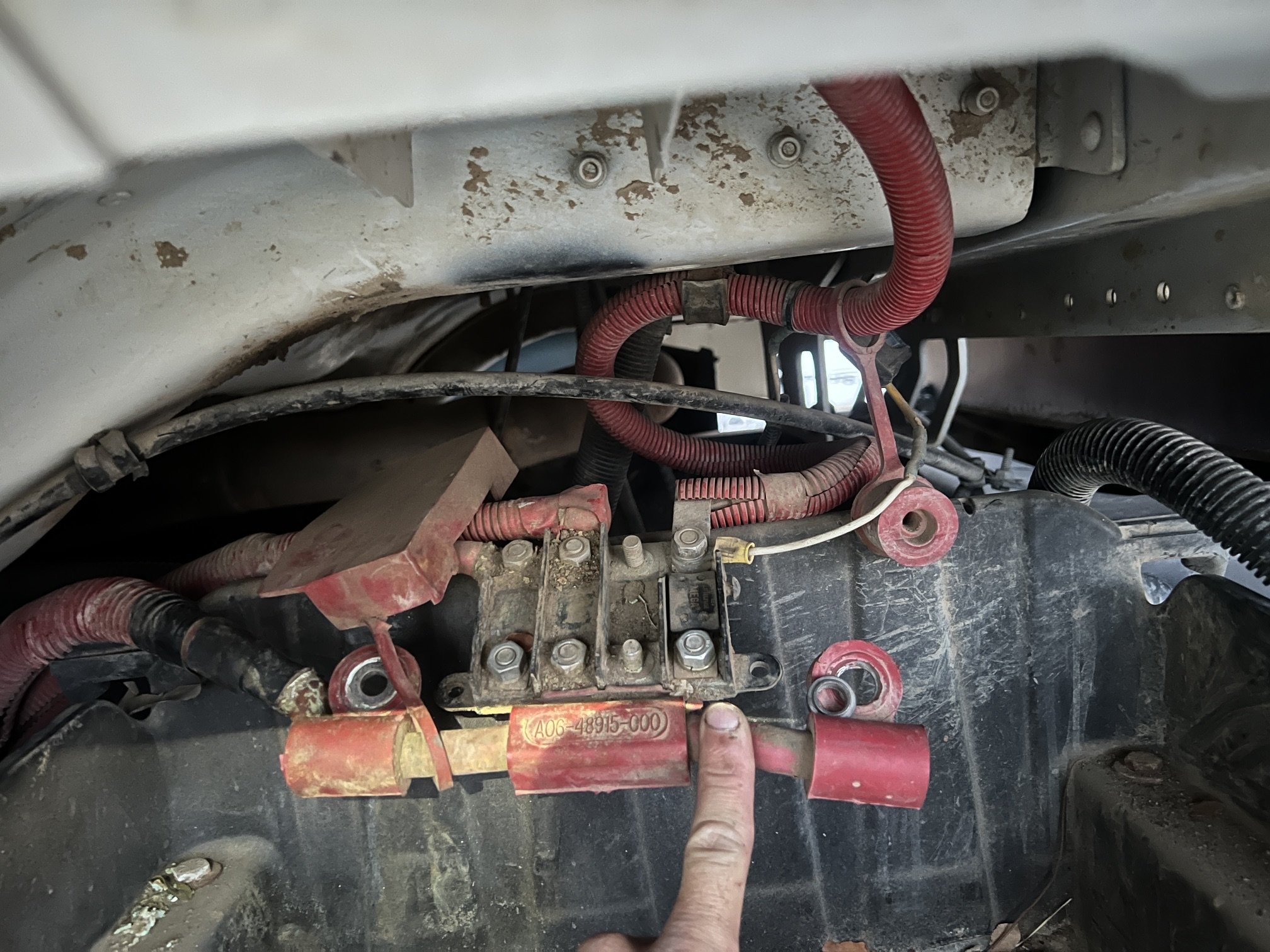 Close-up view of electrical wiring and components inside a vehicle, with a person's finger pointing at a specific part.