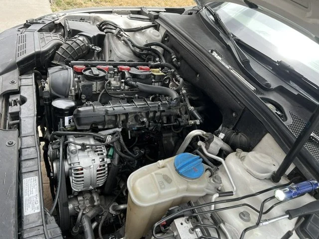Car engine with various hoses, wires, and components visible, including a blue windshield washer fluid cap and a white coolant reservoir.