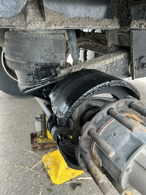 Close-up of a vehicle's wheel hub and suspension, with the wheel removed, showing damaged parts and an automotive jack support underneath.