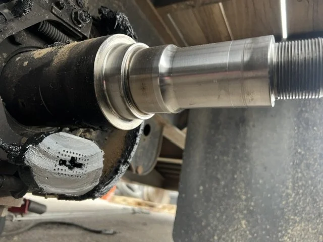 Close-up of a metal shaft with a cylindrical bearing or spacer, mounted in a mechanical assembly, with a threaded end extending outward.