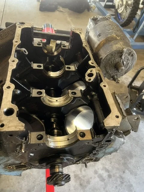 Open engine cylinder head with visible pistons, camshaft, and other internal components, with a starter motor mounted on the top right outside of the engine block.