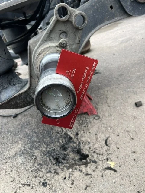 Close-up of a motorcycle front fork with a red business card attached, showing the wheel mounted without the tire, revealing the wheel's hub and spokes.