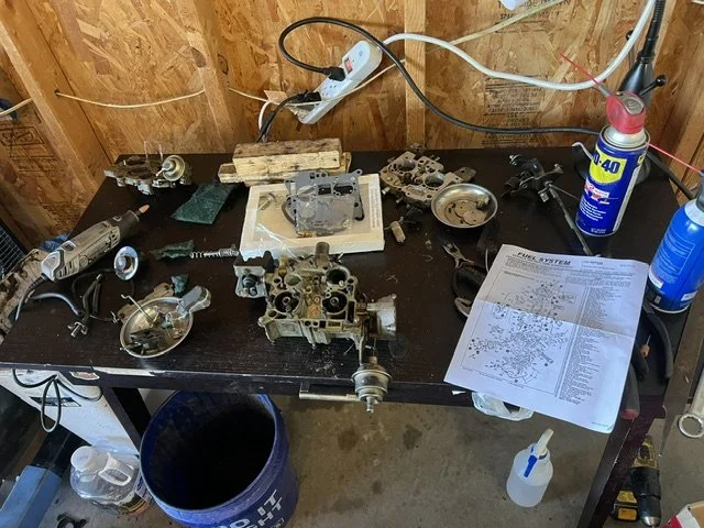 A workbench with disassembled engine parts, tools, a manual, and cleaning supplies in a garage workshop.