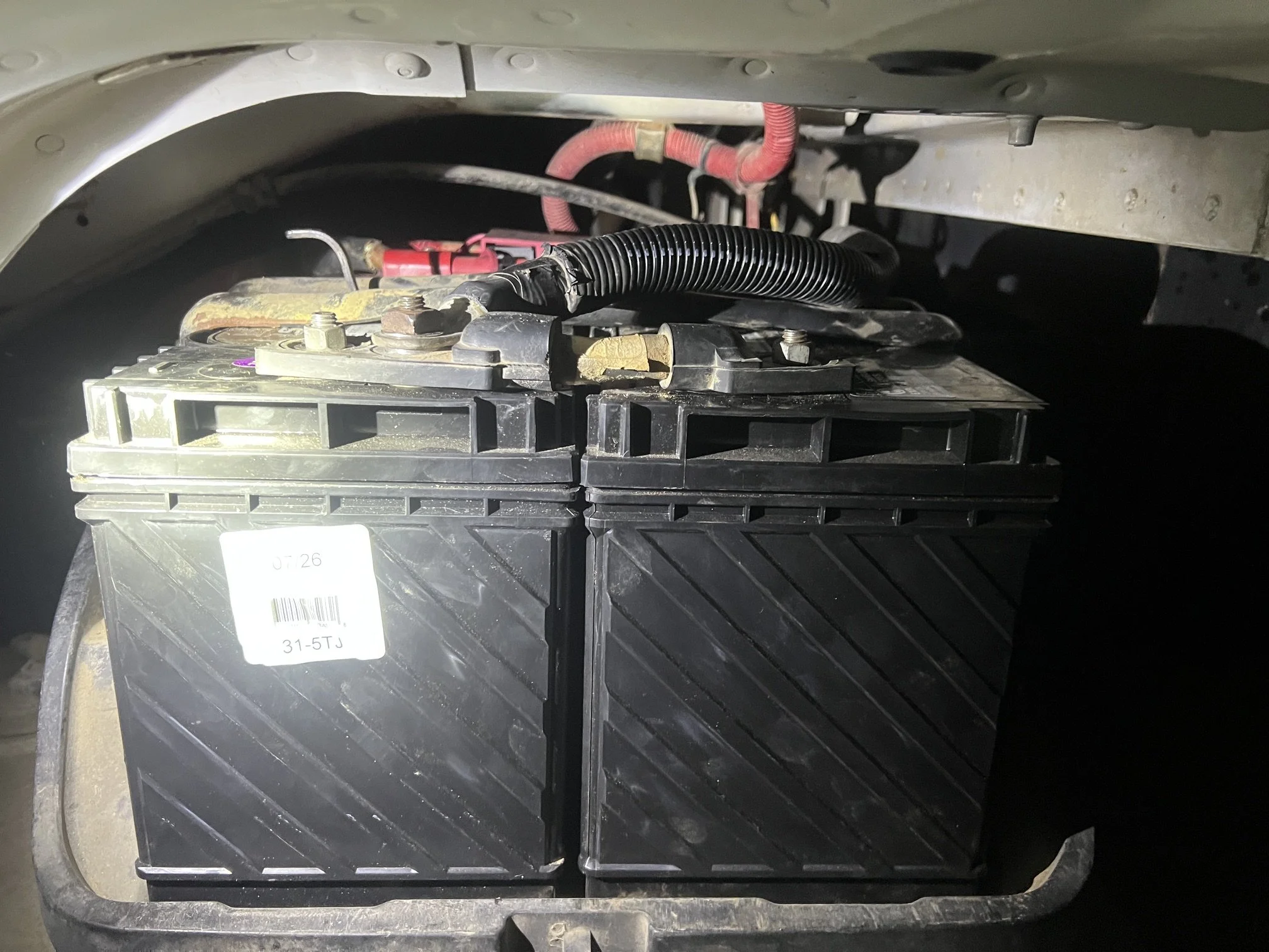 A vehicle battery with visible terminals connected by cables inside the engine compartment.