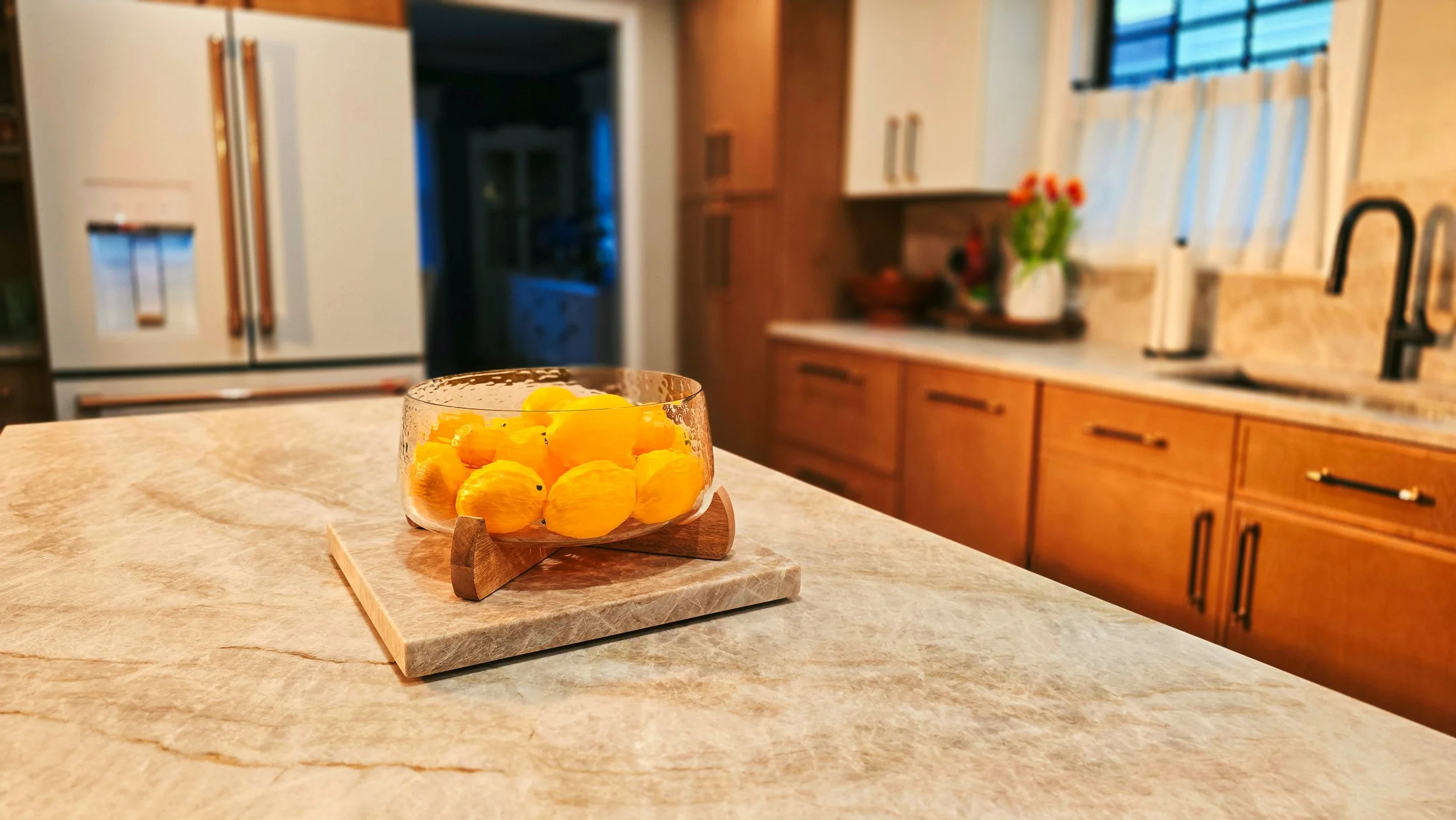 A clear glass bowl filled with yellow chick-shaped candies sits on a wooden stand on a kitchen counter.