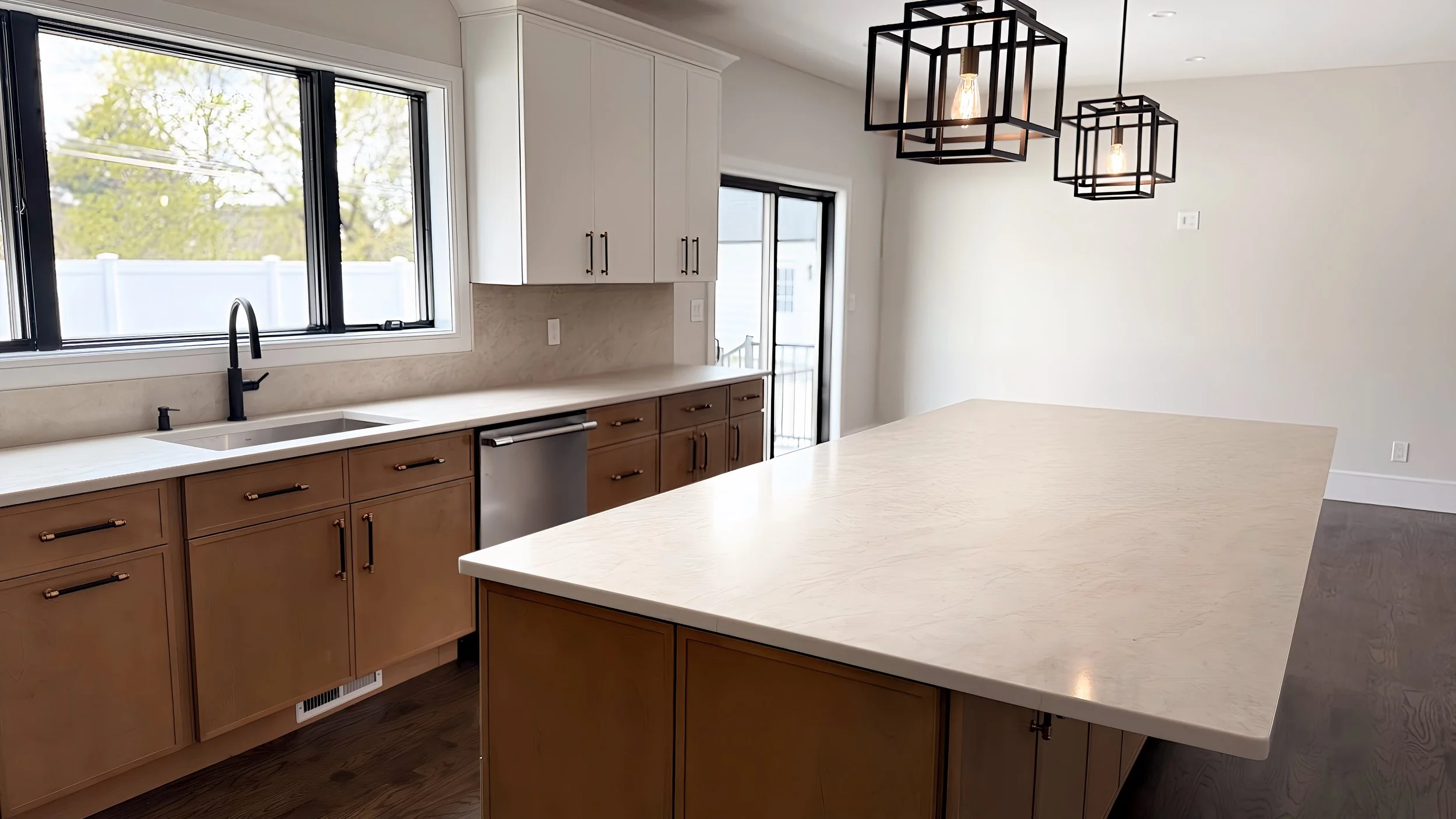Modern kitchen with large white island, wooden cabinets, black faucet, and pendant lights with geometric frames hanging from the ceiling.