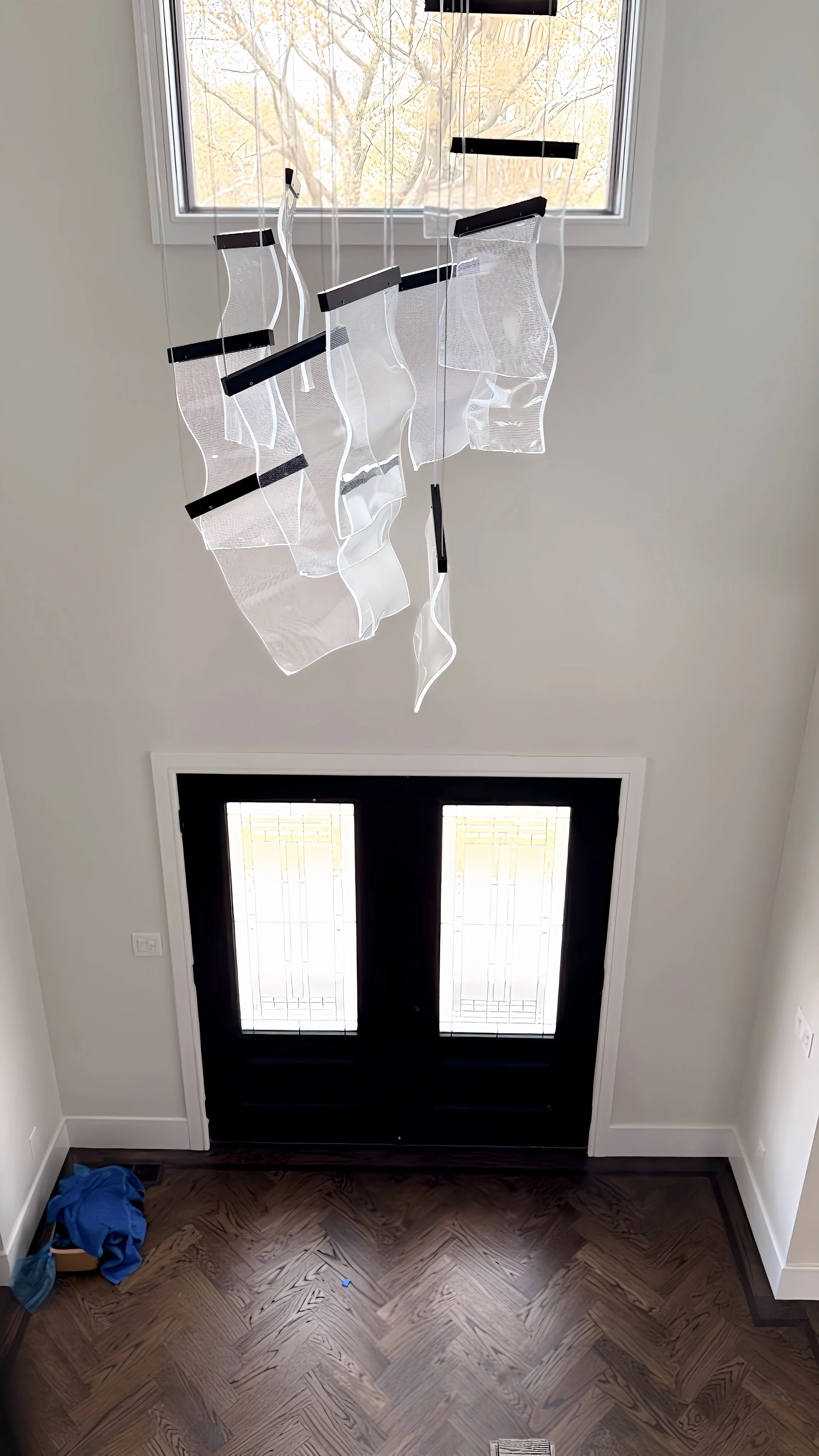 Front door with decorative glass panels, white walls, and a modern light fixture hanging from a window ceiling.