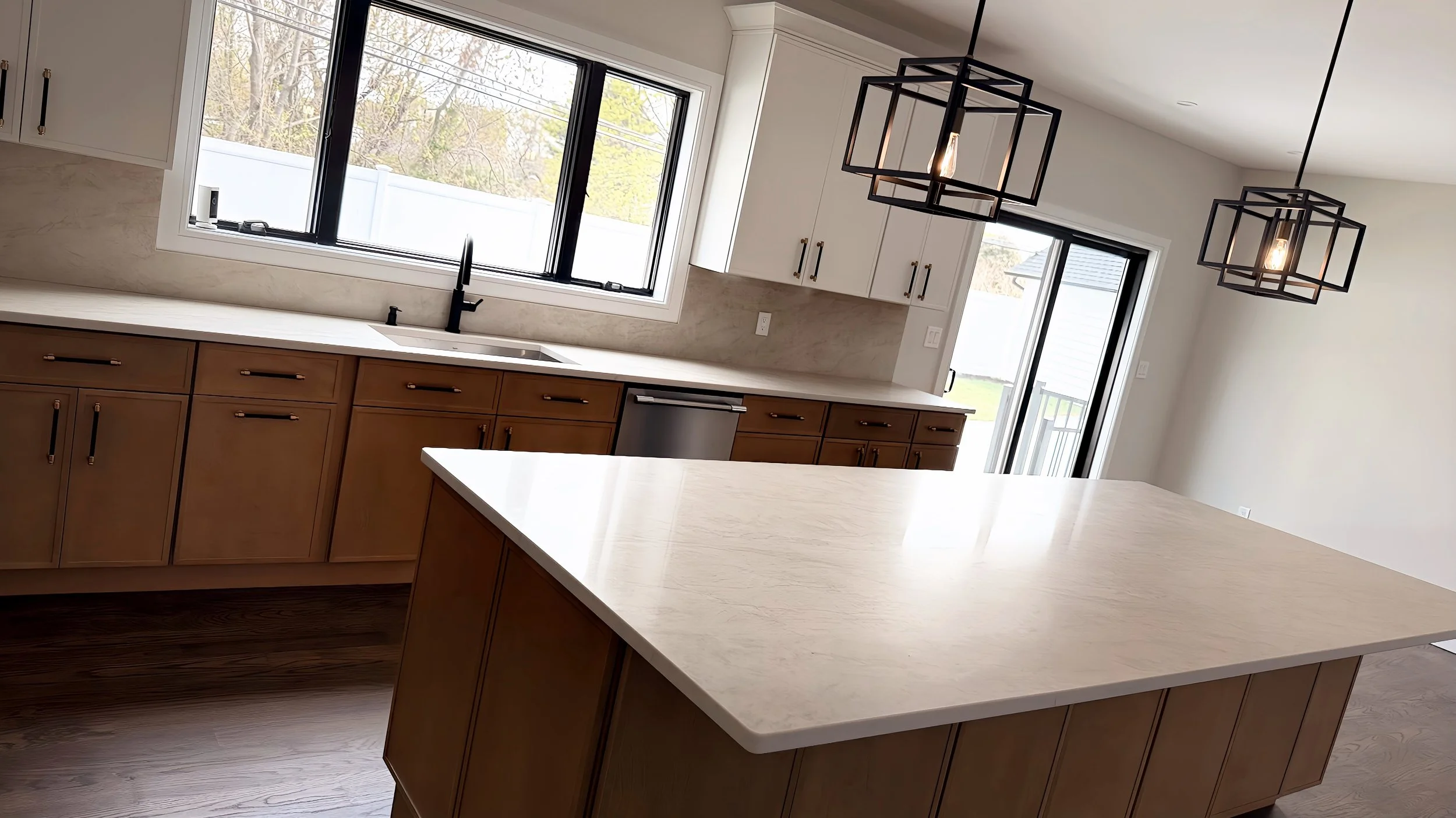 Modern kitchen with white cabinets, a large window above the sink, black fixtures, and two black geometric pendant lights hanging from the ceiling.