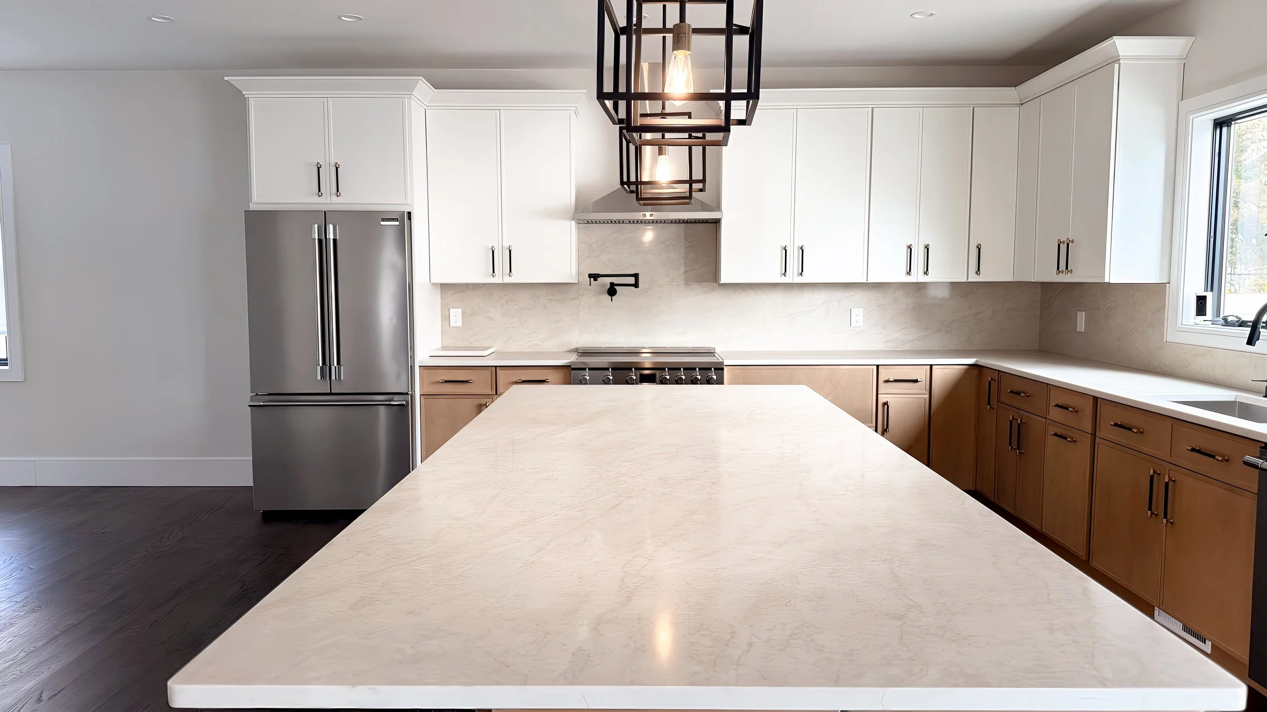 Modern kitchen with white cabinets, a marble backsplash, a stainless steel refrigerator, a stovetop under a range hood, a unique black pendant light, and a kitchen island with a marble countertop.