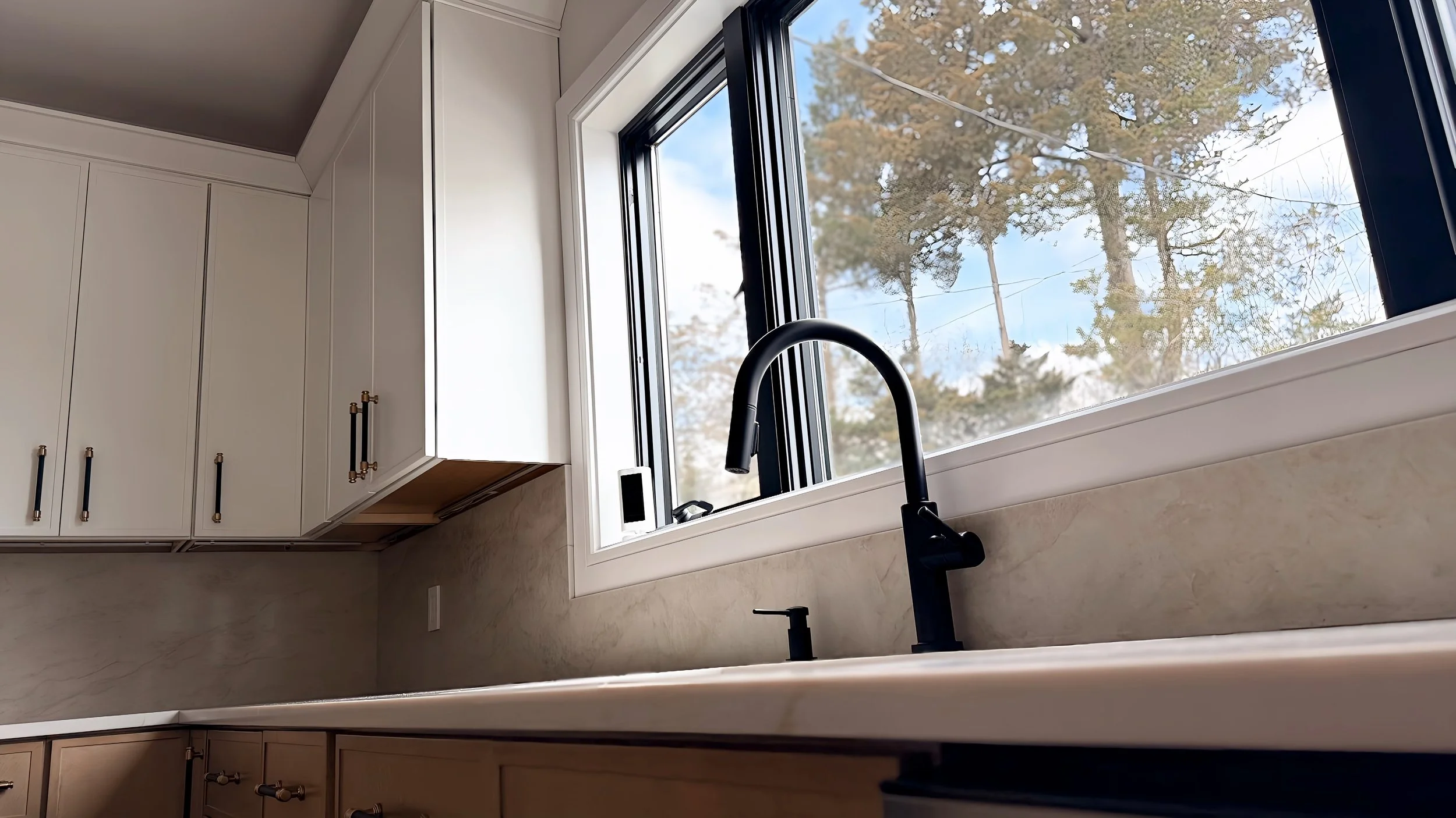 Kitchen with white cabinets, a black kitchen faucet, and a large window showing trees outside.