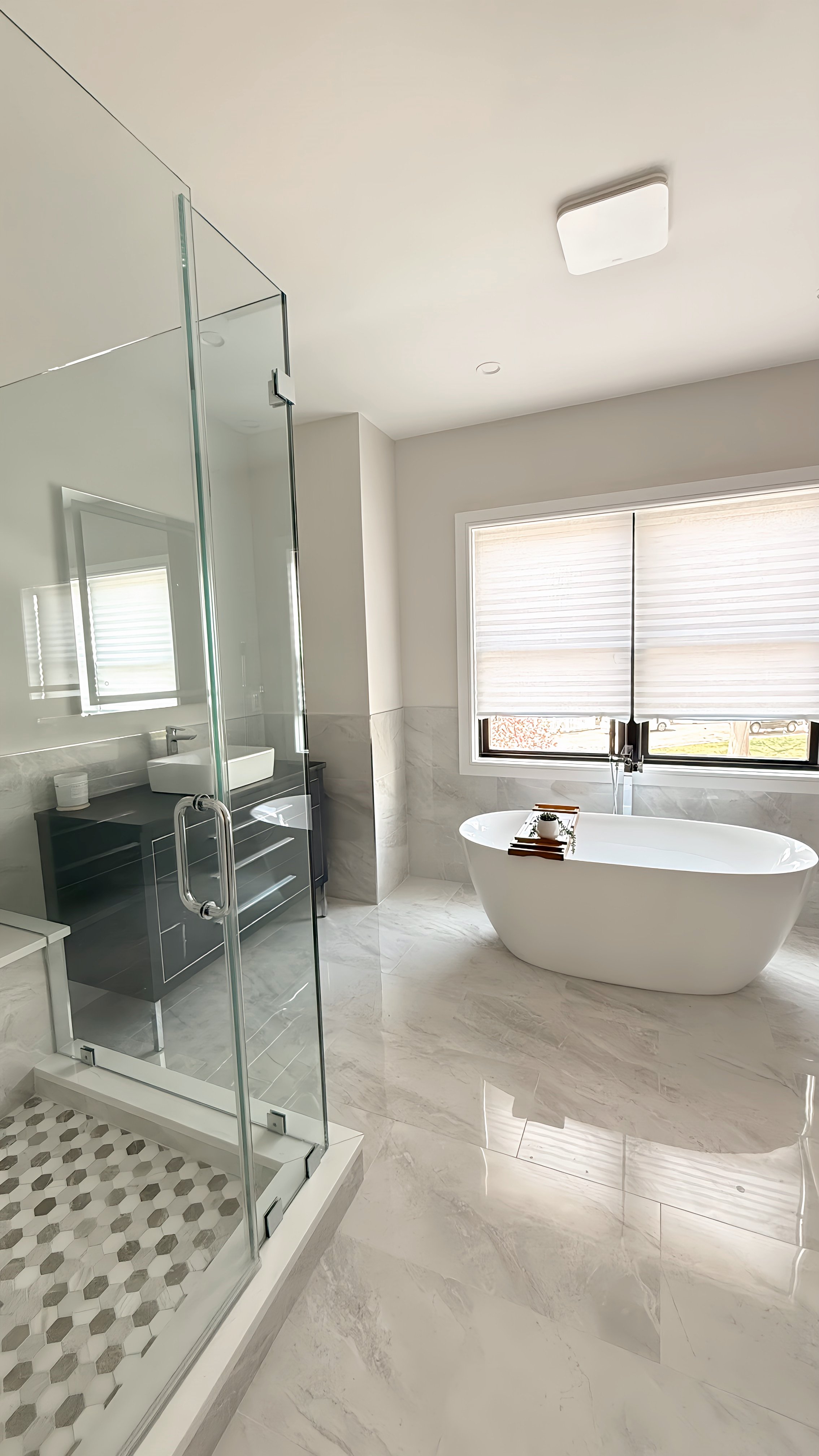 Modern bathroom with a glass-enclosed shower, a freestanding bathtub near a window, and a black vanity with a white sink.