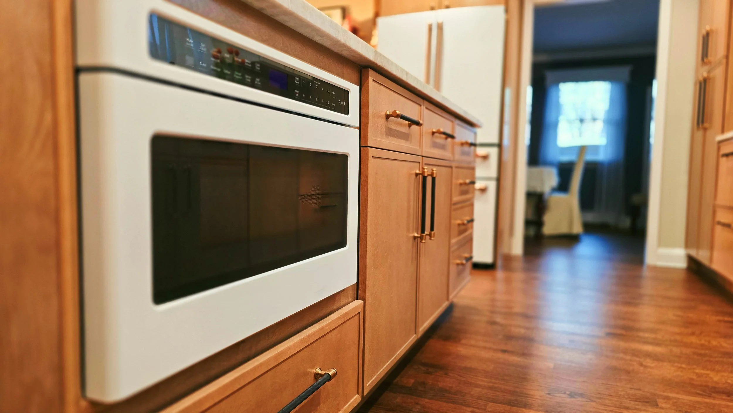 View of a kitchen with wooden cabinets, a white oven, and a window in the background with blue curtains.
