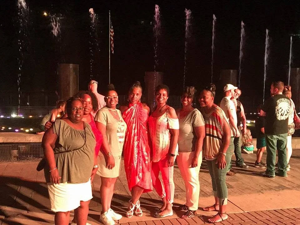 A group of women standing in front of a water fountain at night, smiling and posing for the photo.