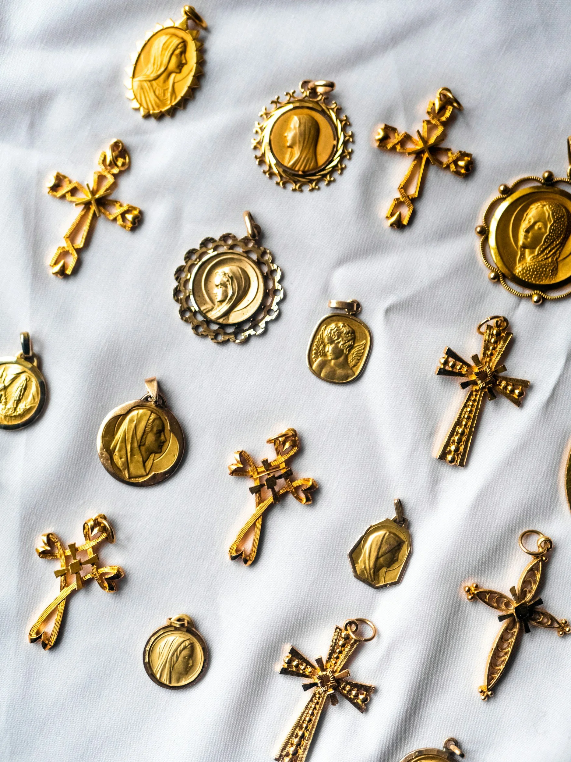 Gold religious medallions and crosses arranged on a white fabric background.