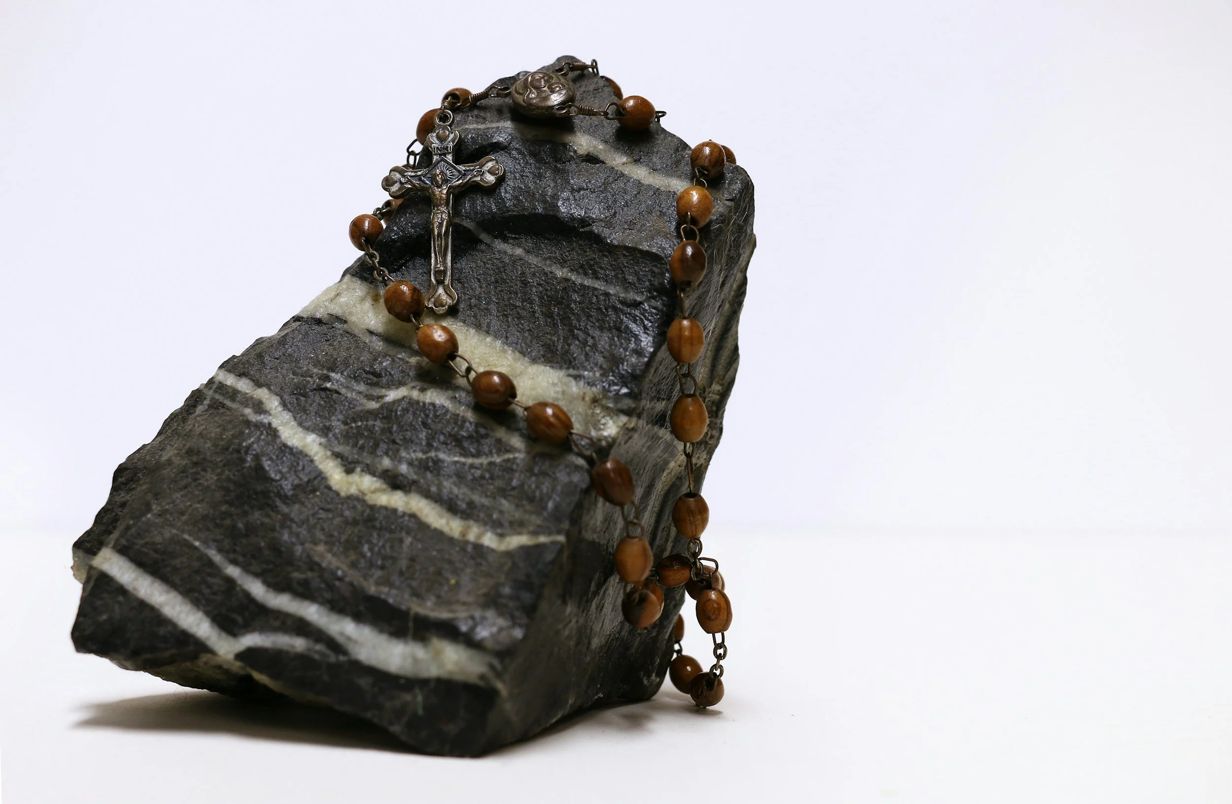 A rosary with brown beads and a metal crucifix draped over a black and white striped stone.