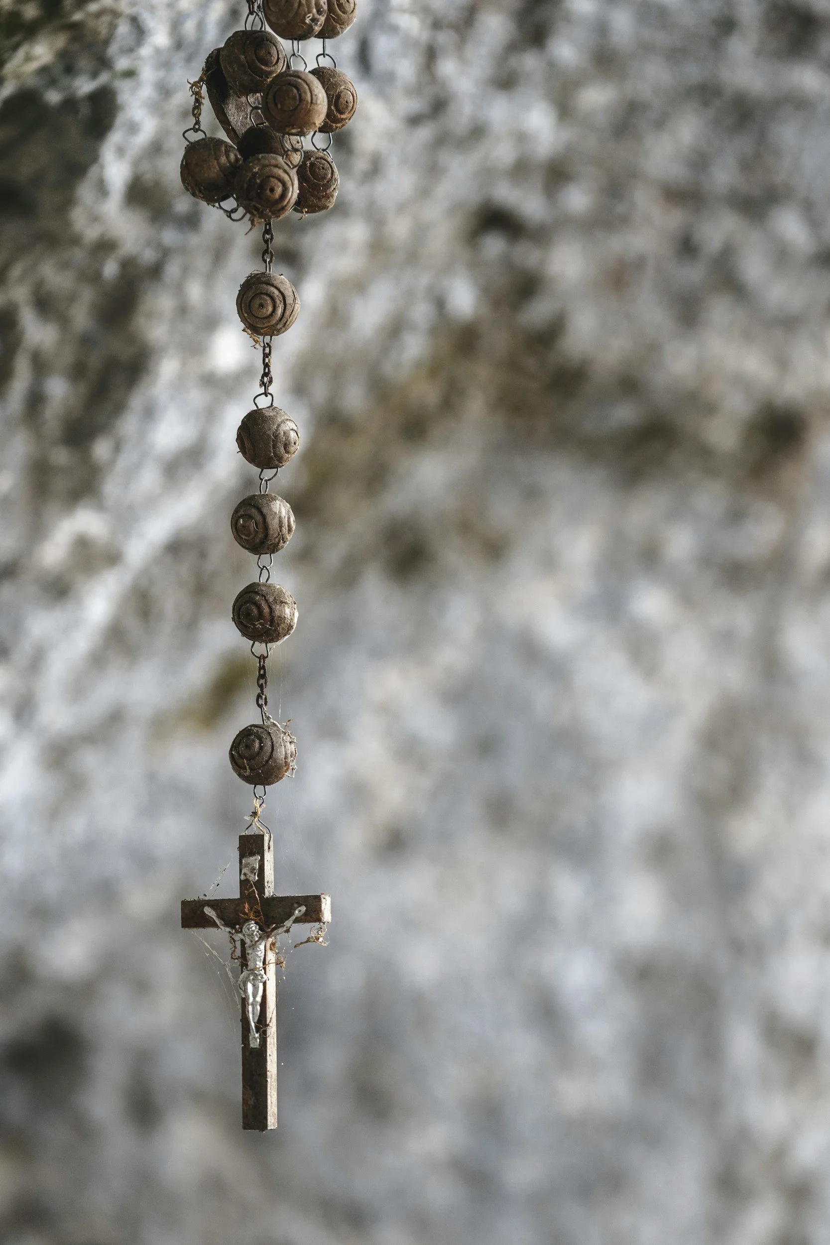 Close-up of a hanging cross with beaded decoration, against a blurred natural background.