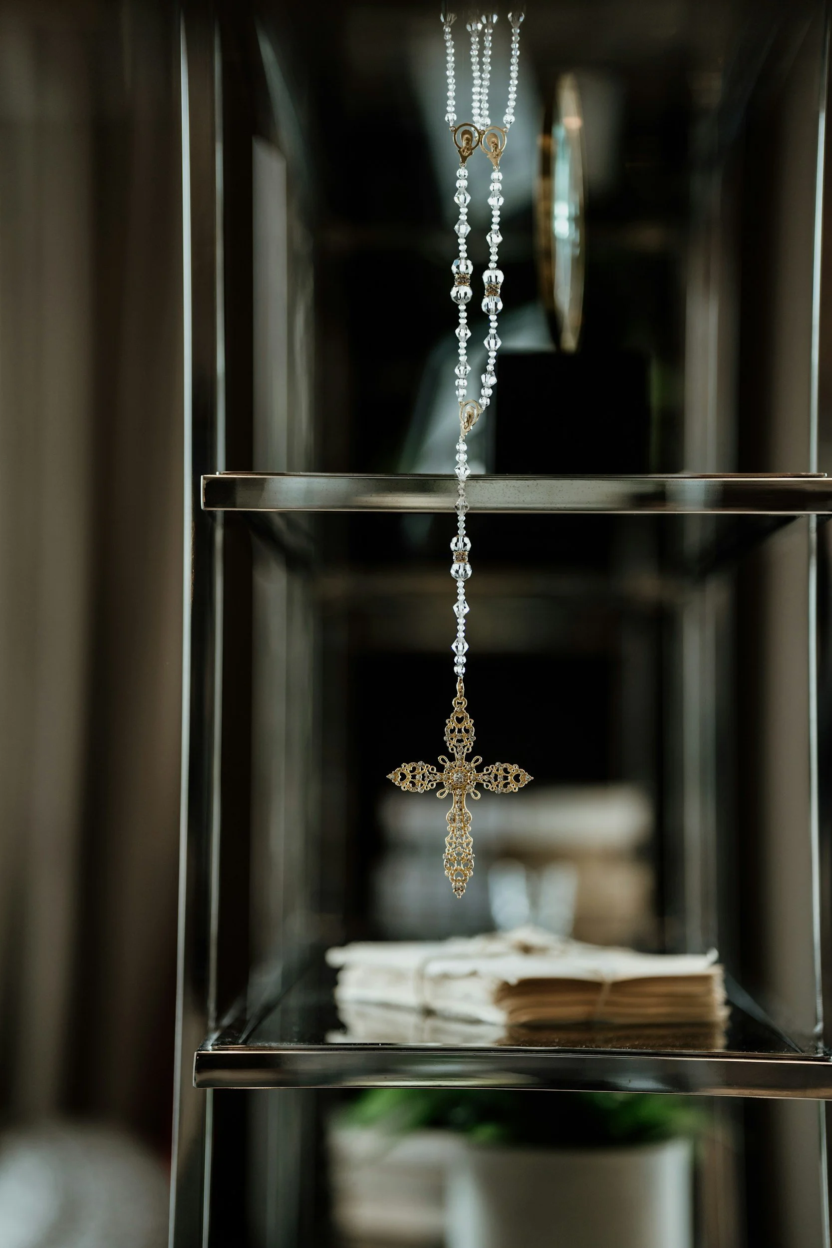 A chandelier with dangling clear beads and a gold cross pendant hangs inside a display case, with an open book underneath.