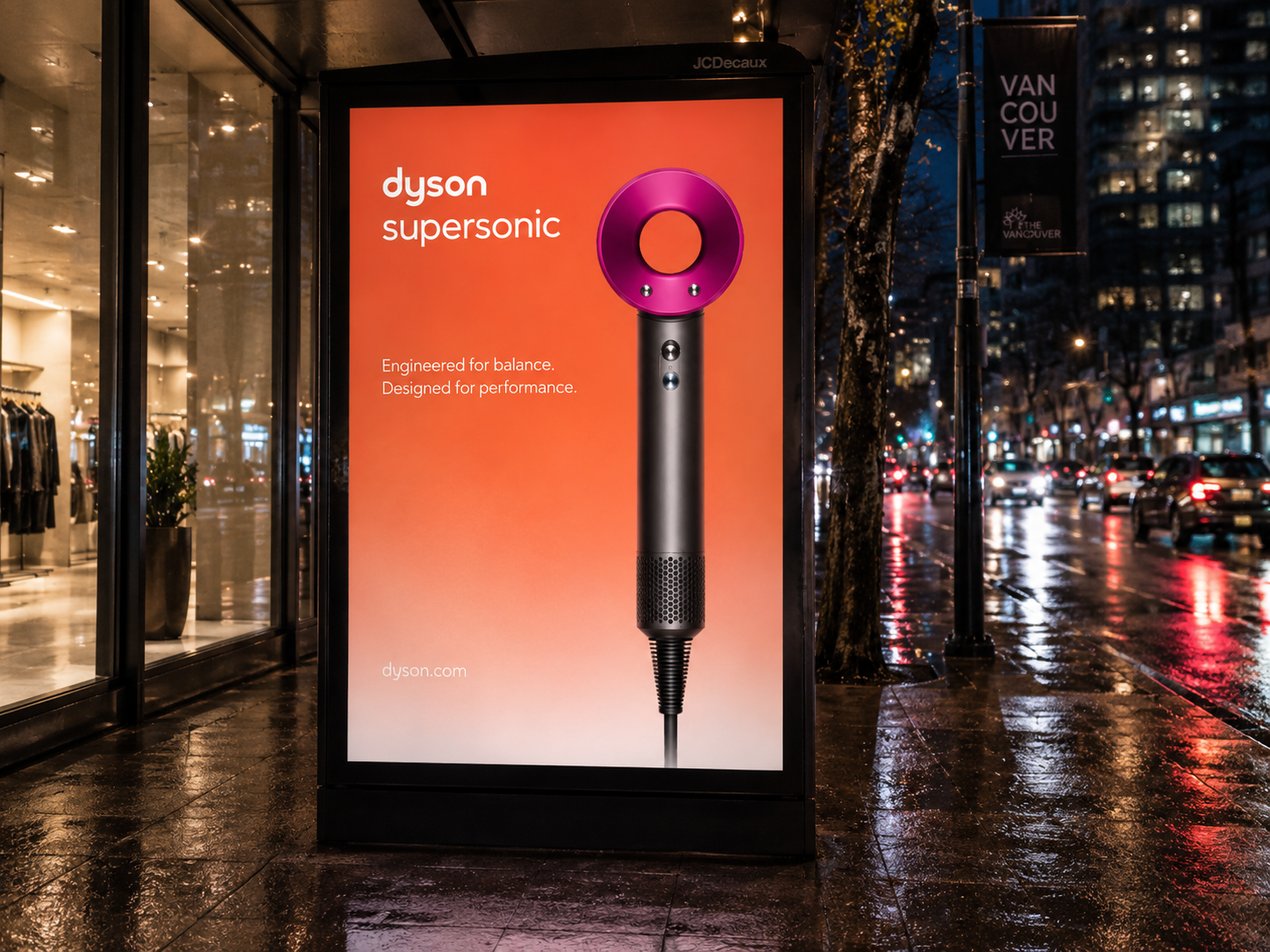 Advertising poster for Dyson Supersonic hair dryer on a city sidewalk at night, with rain and illuminated buildings in the background.