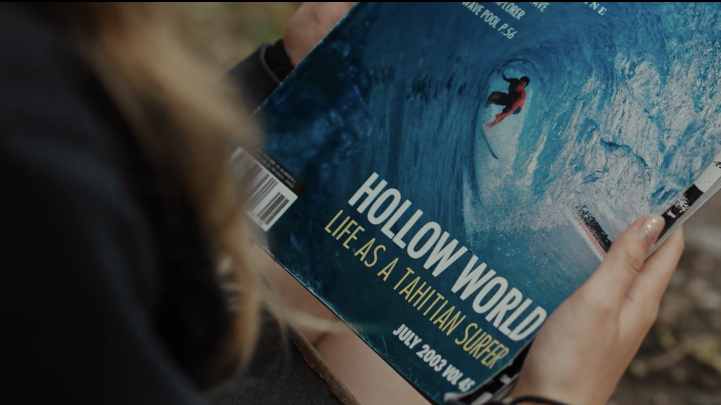 Close-up of a person holding a magazine titled 'Hollow World: Life as a Tahitian Surfer,' featuring a person surfing on a large wave.