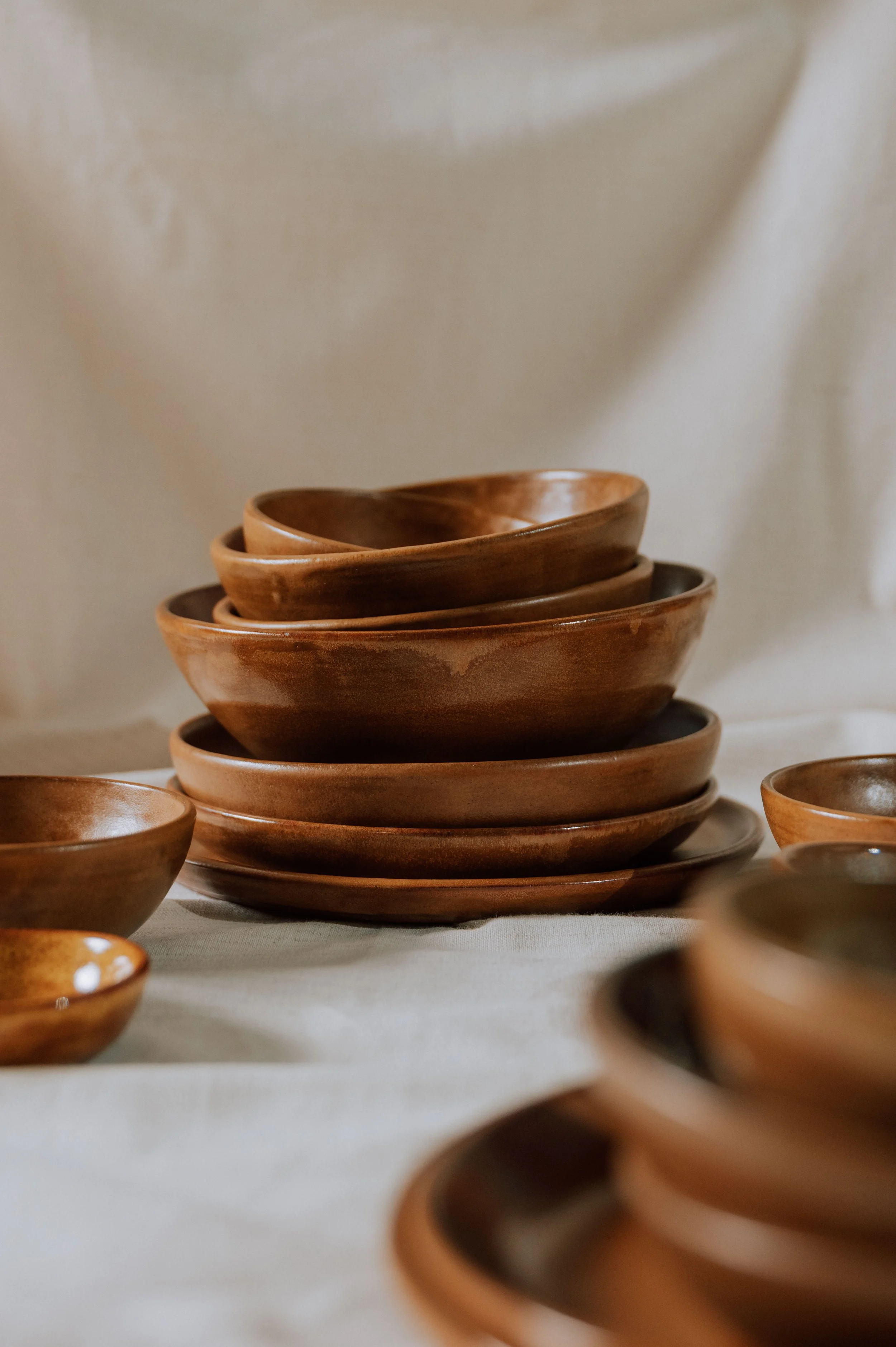Stack of handmade brown ceramic bowls and plates on a linen-covered table