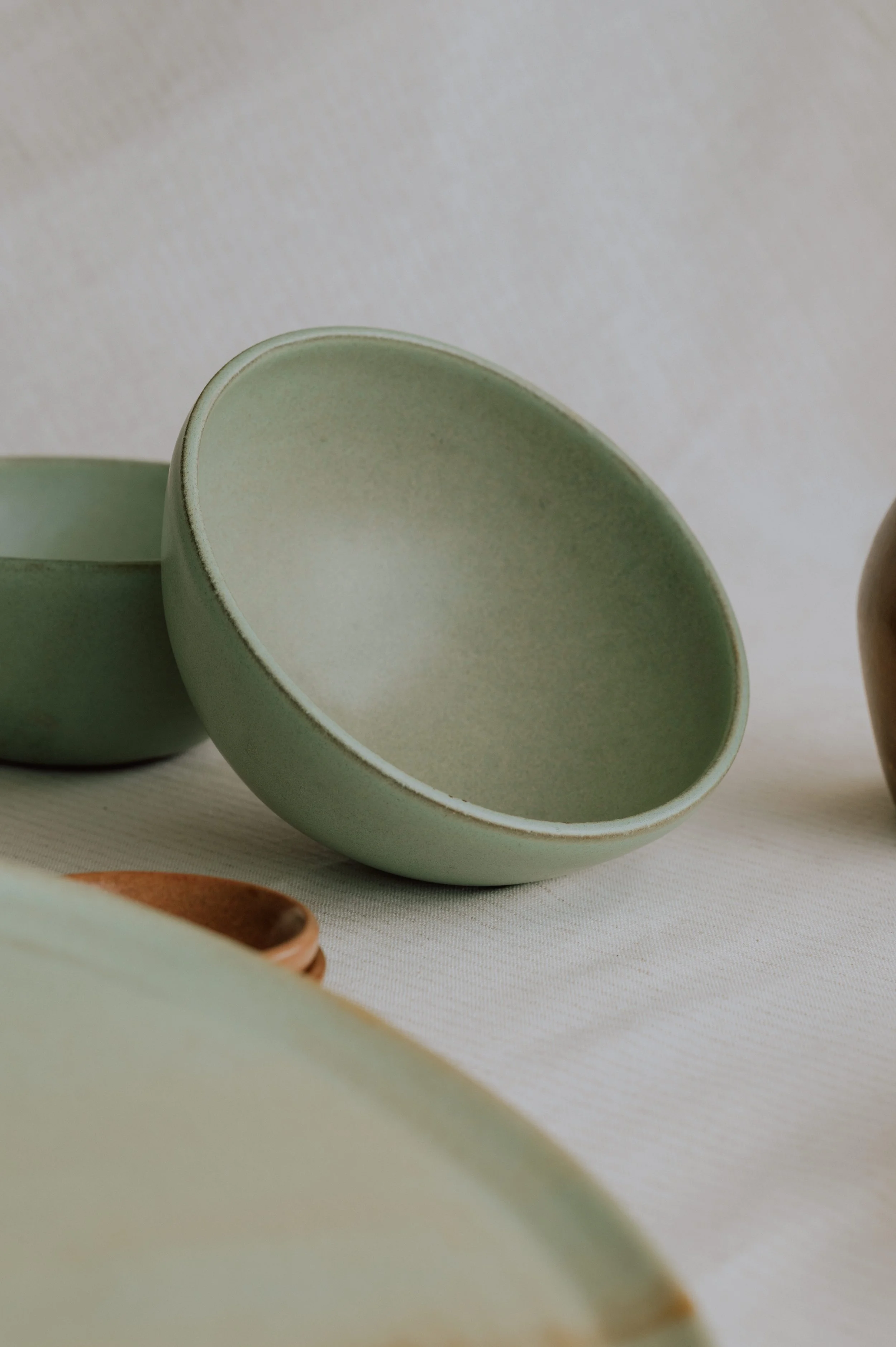 Matte sage green ceramic bowl displayed on a neutral linen surface with minimalist tableware.
