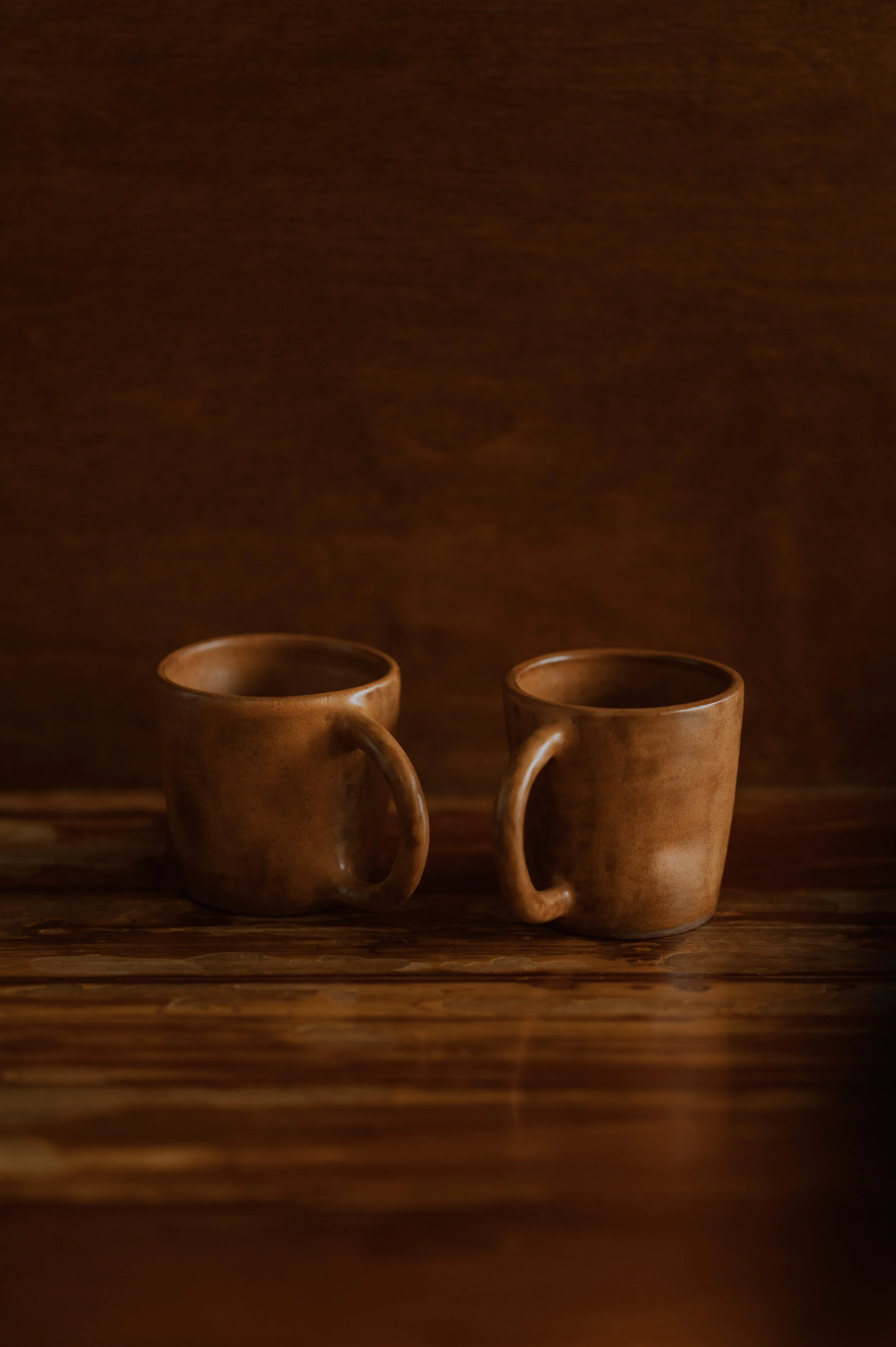 handmade brown ceramic cups with handles in a wooden background