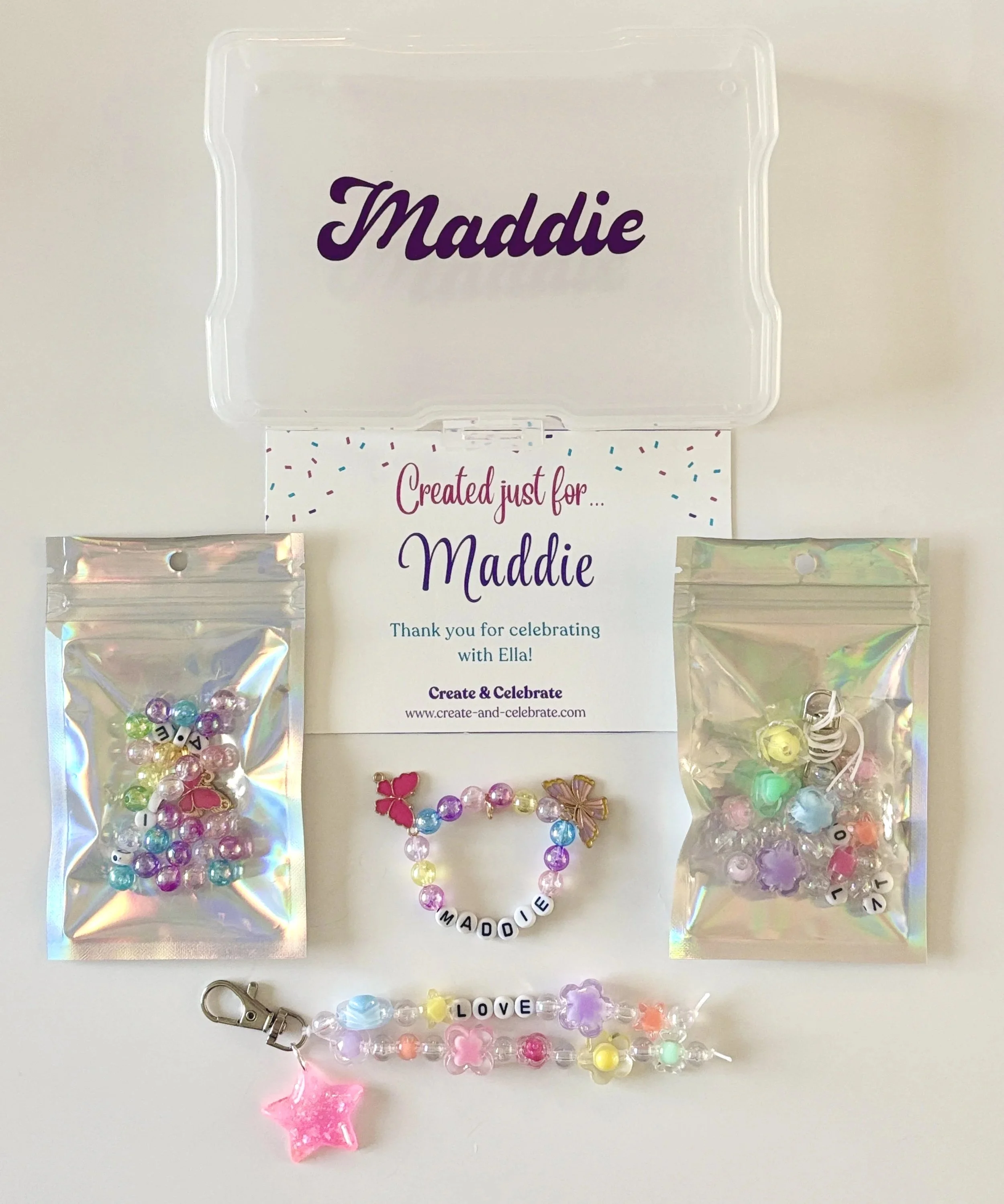 Jewelry pieces on clear plastic bags, including beaded bracelets with lettered charms spelling out 'MADDIE' and 'LOVE', and a pink star-shaped pendant with a pink ribbon charm, arranged on a white surface with a card thanking for celebrating with Ell
