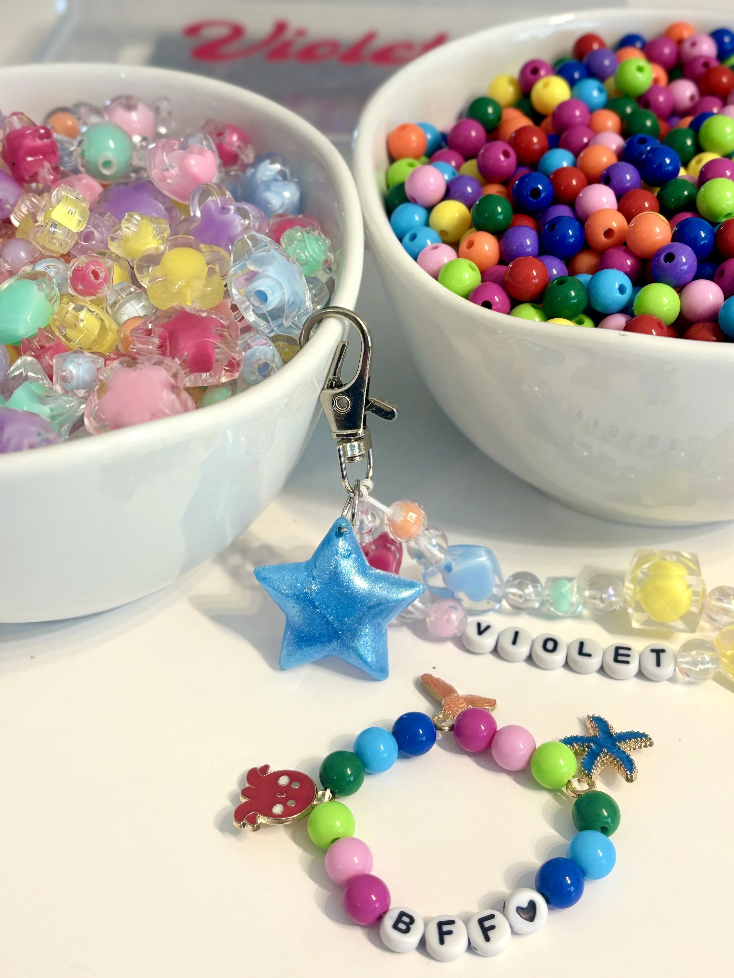 Colorful beaded jewelry pieces including a blue star-shaped pendant and a red fruit-shaped charm, with two bowls of assorted colorful beads in the background.