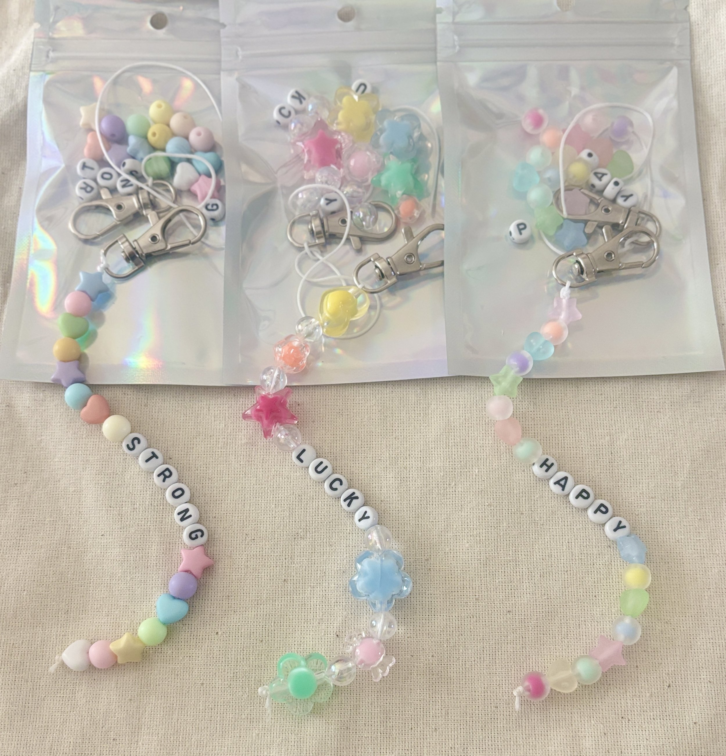 Complicated set of pastel-colored beaded keychains, each with a small metal clasp, displayed on a holographic surface.
