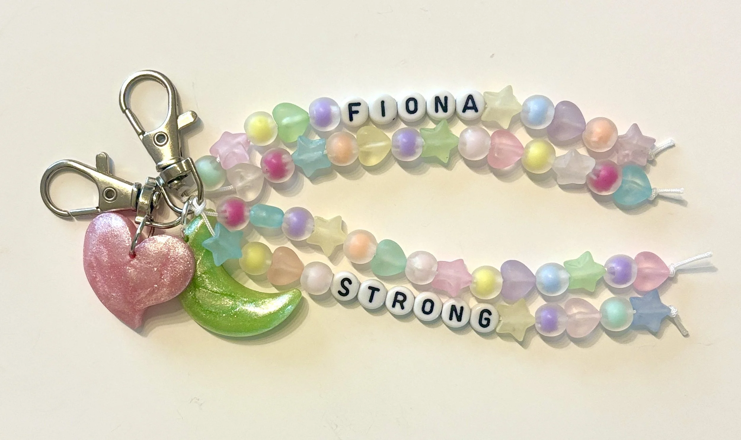 Colorful beaded keychain with pink heart, green leaf, and beads spelling 'FIONA STRONG'