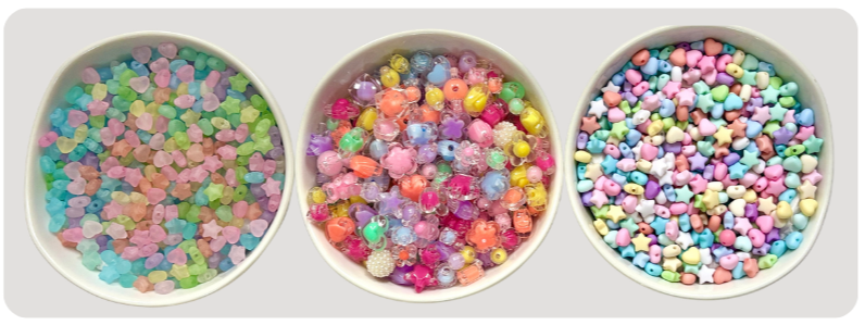 Three small white bowls filled with colorful sugar beads, decorations, and tiny plastic beads for crafting or baking.
