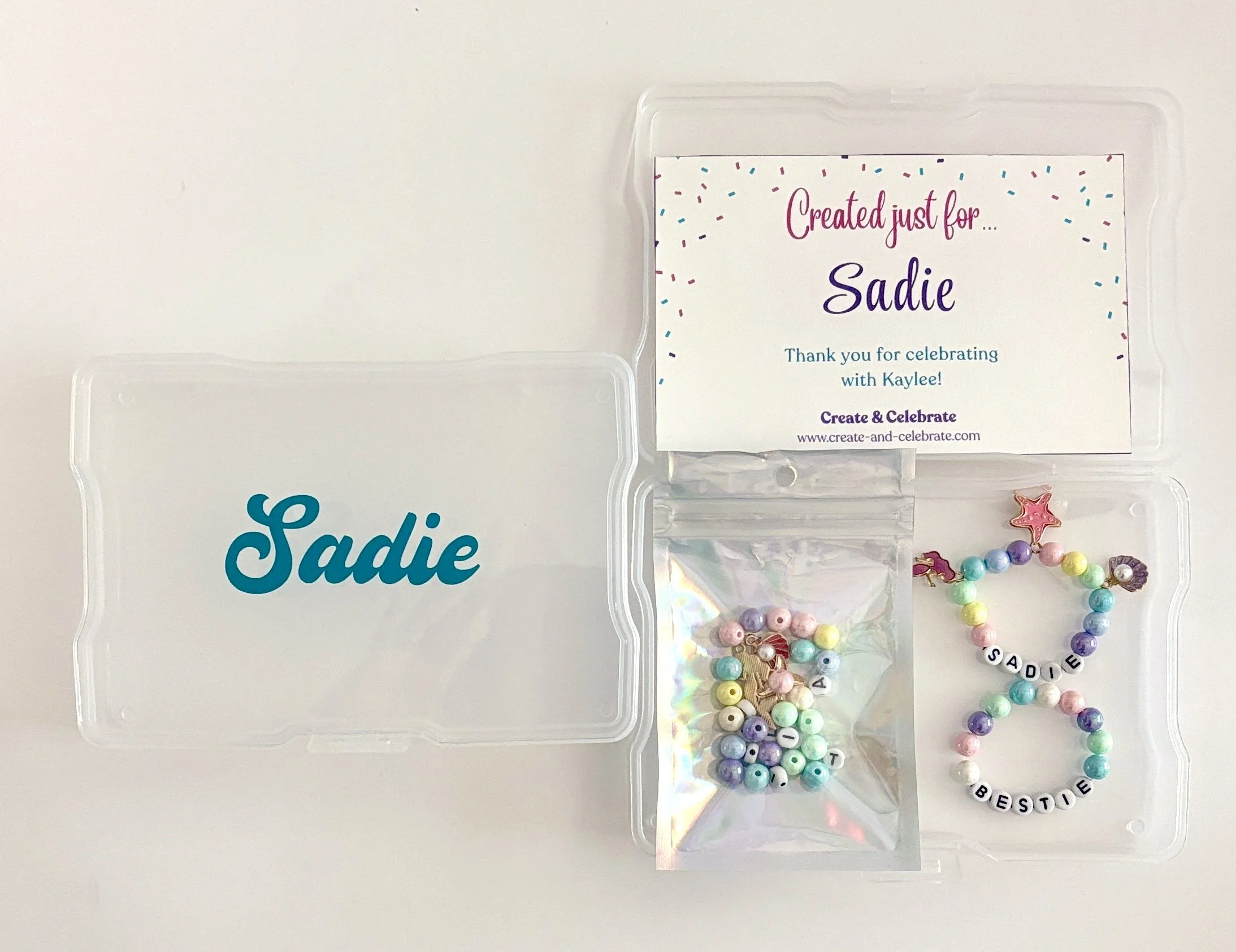 A clear plastic container with a label reading, 'Created just for... Sadie,' and colorful beaded jewelry in pastel shades, with some beads spelling out ''Sadie'' and ''Bestie''.
