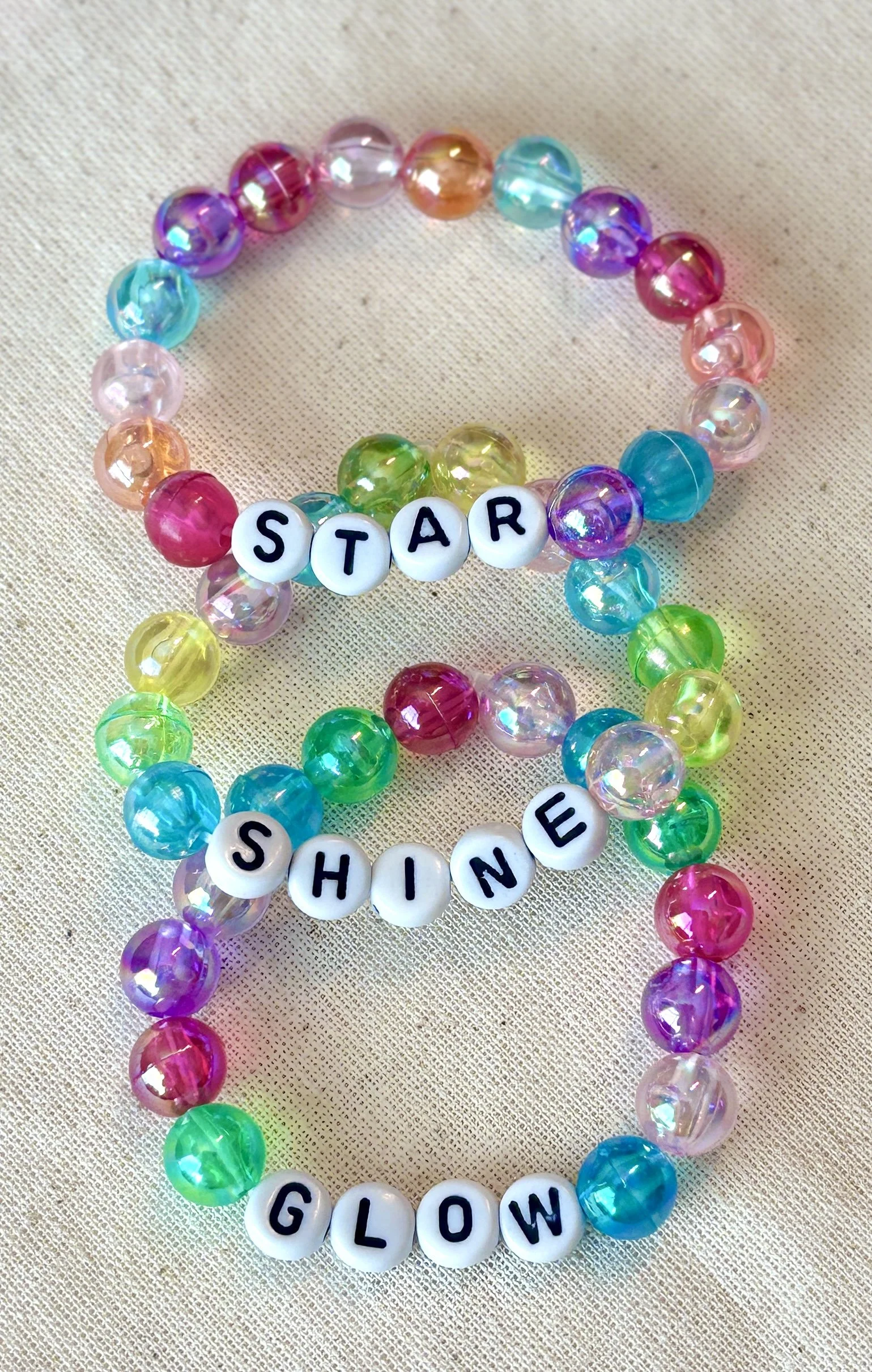 Colorful beaded bracelets spelling out 'STAR SHINE GLOW' on a fabric background.