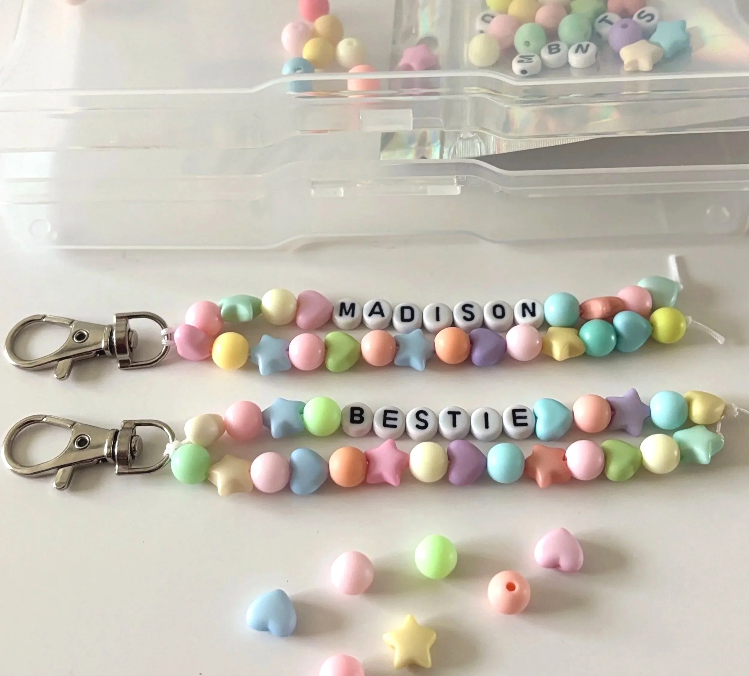 Colorful beaded jewelry with letter beads spelling 'MADISON' and 'BESIDE' displayed on a white surface, with a plastic container in the background.