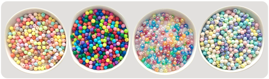 Four white bowls filled with colorful small beads and pearls, arranged in a row on a white background.