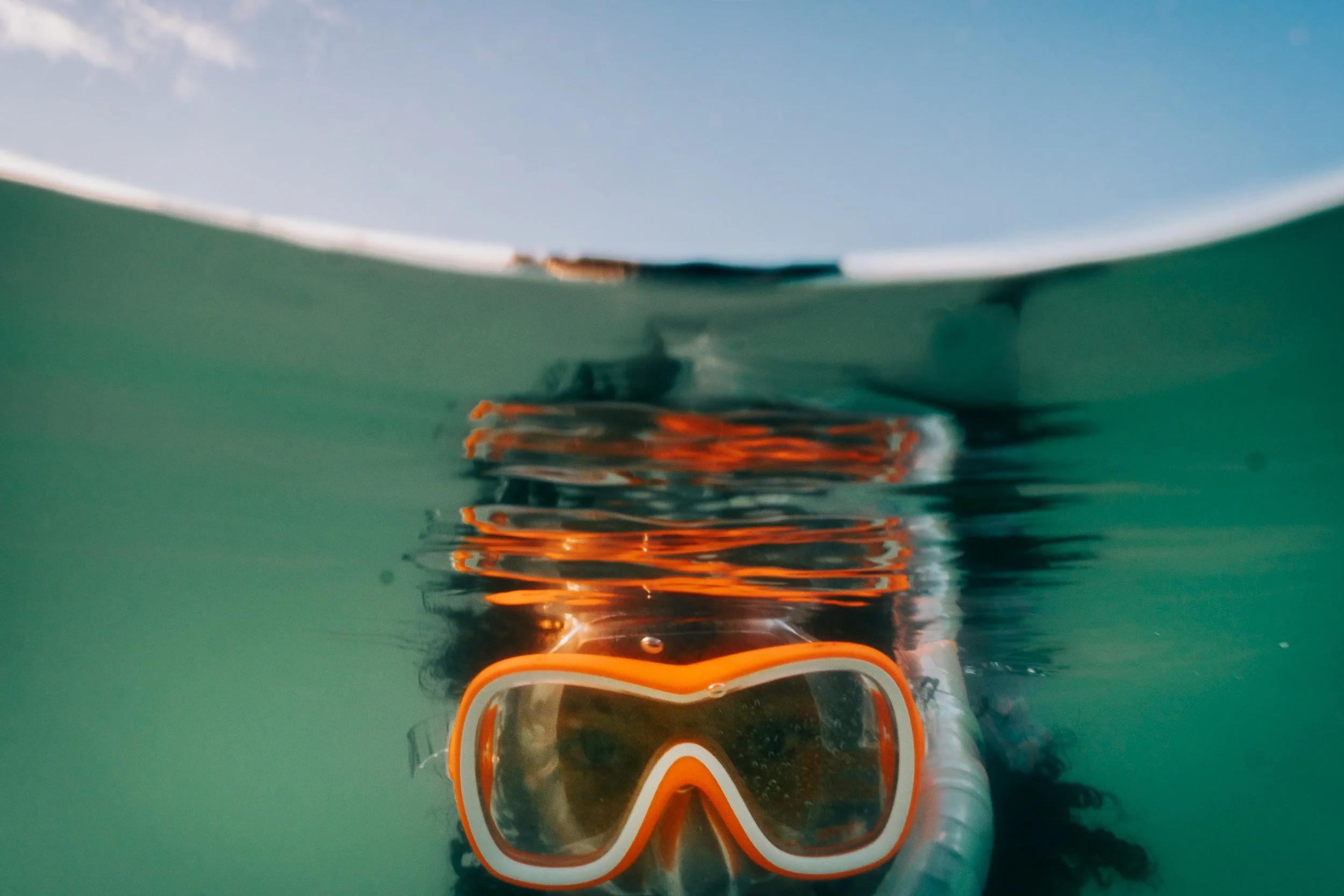 A person underwater wearing orange snorkeling gear, looking up at the surface.