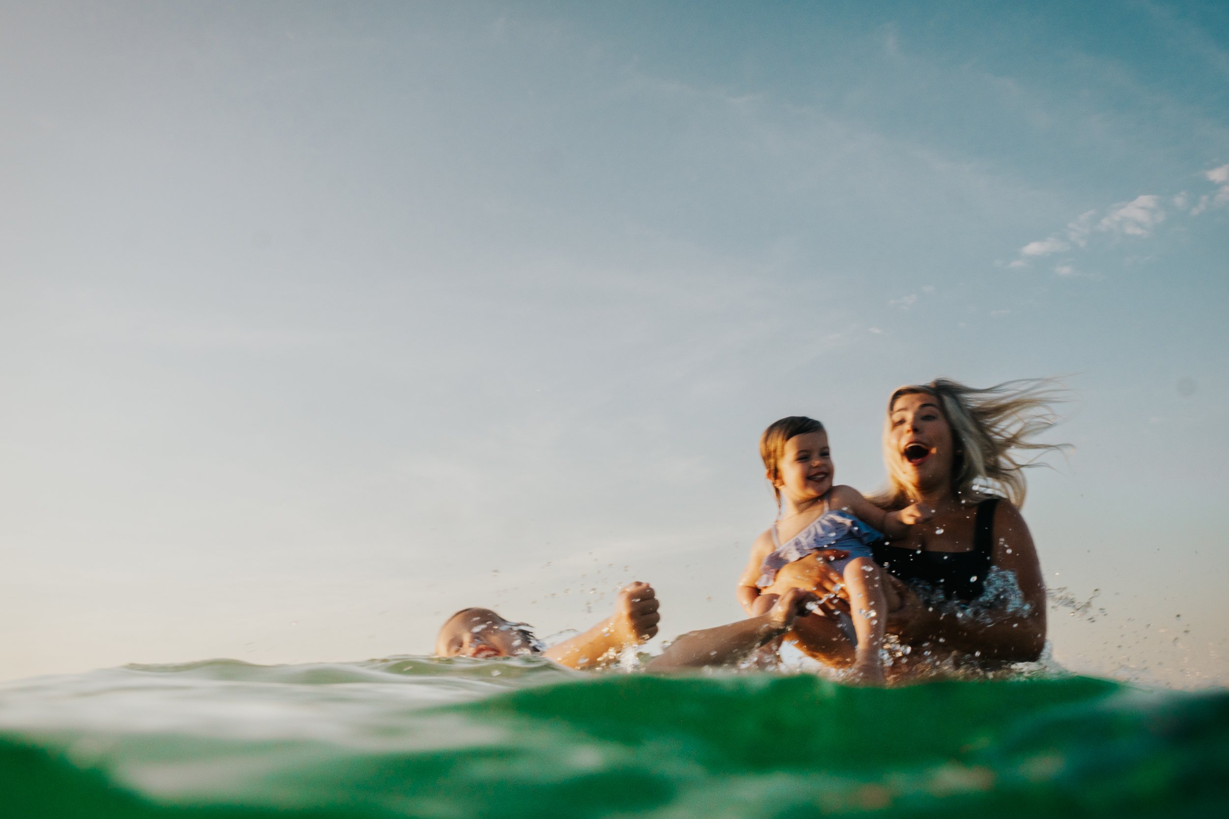 A woman and a young girl playing and splashing in the water at the beach during sunset.