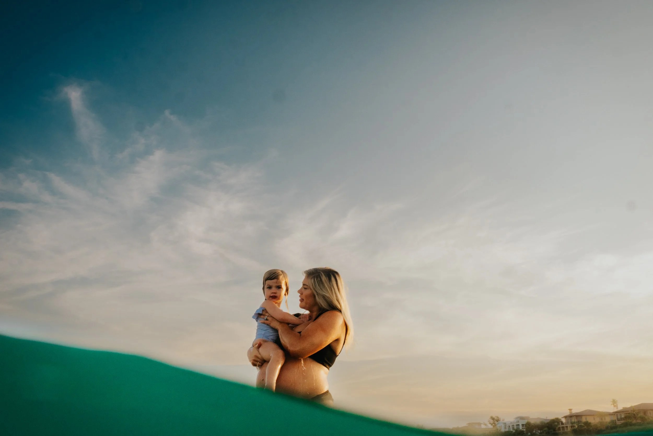A woman holding a young child outdoors with a cloudy sky at sunset in the background.