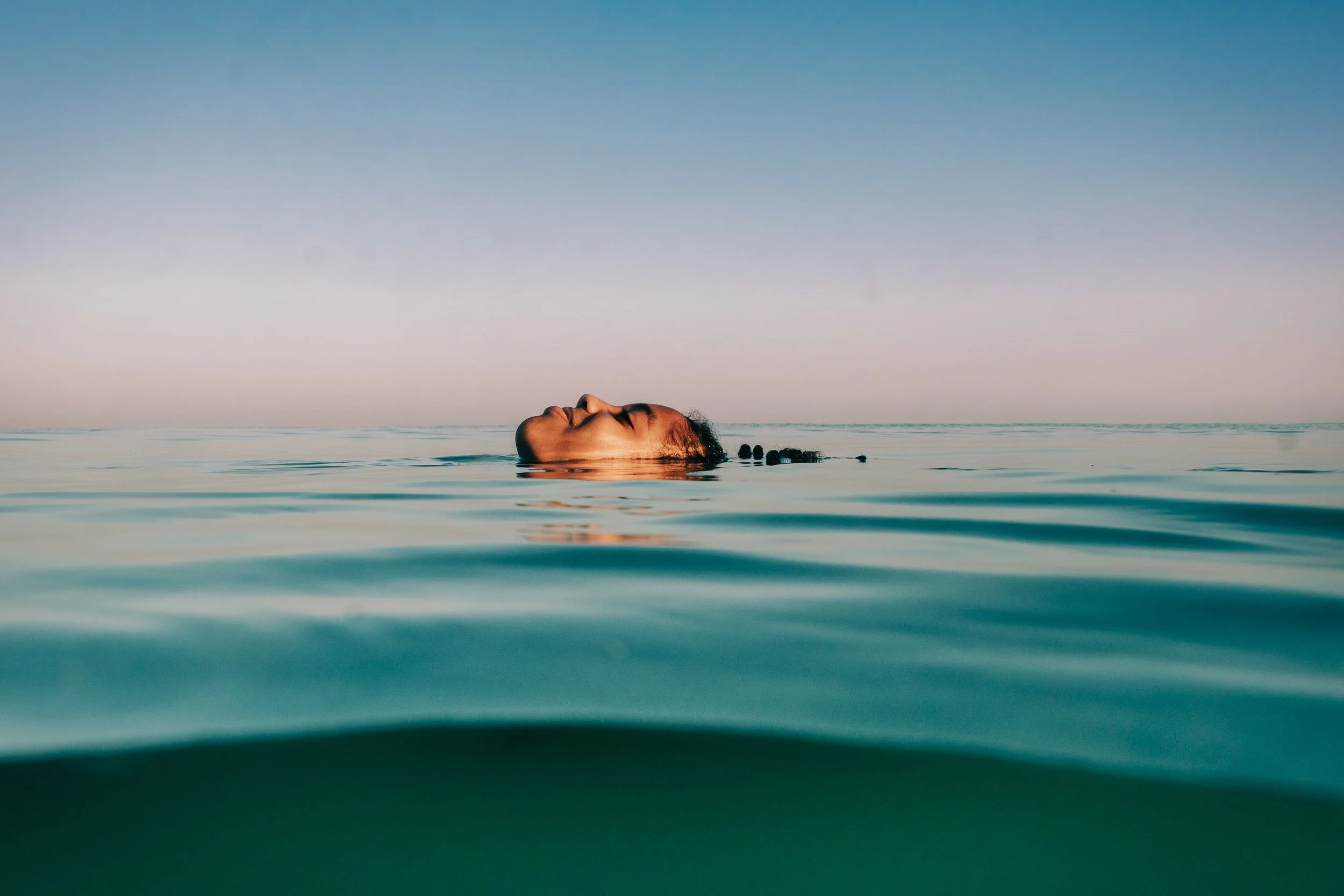 Person with long hair floating in calm ocean water with clear sky above.