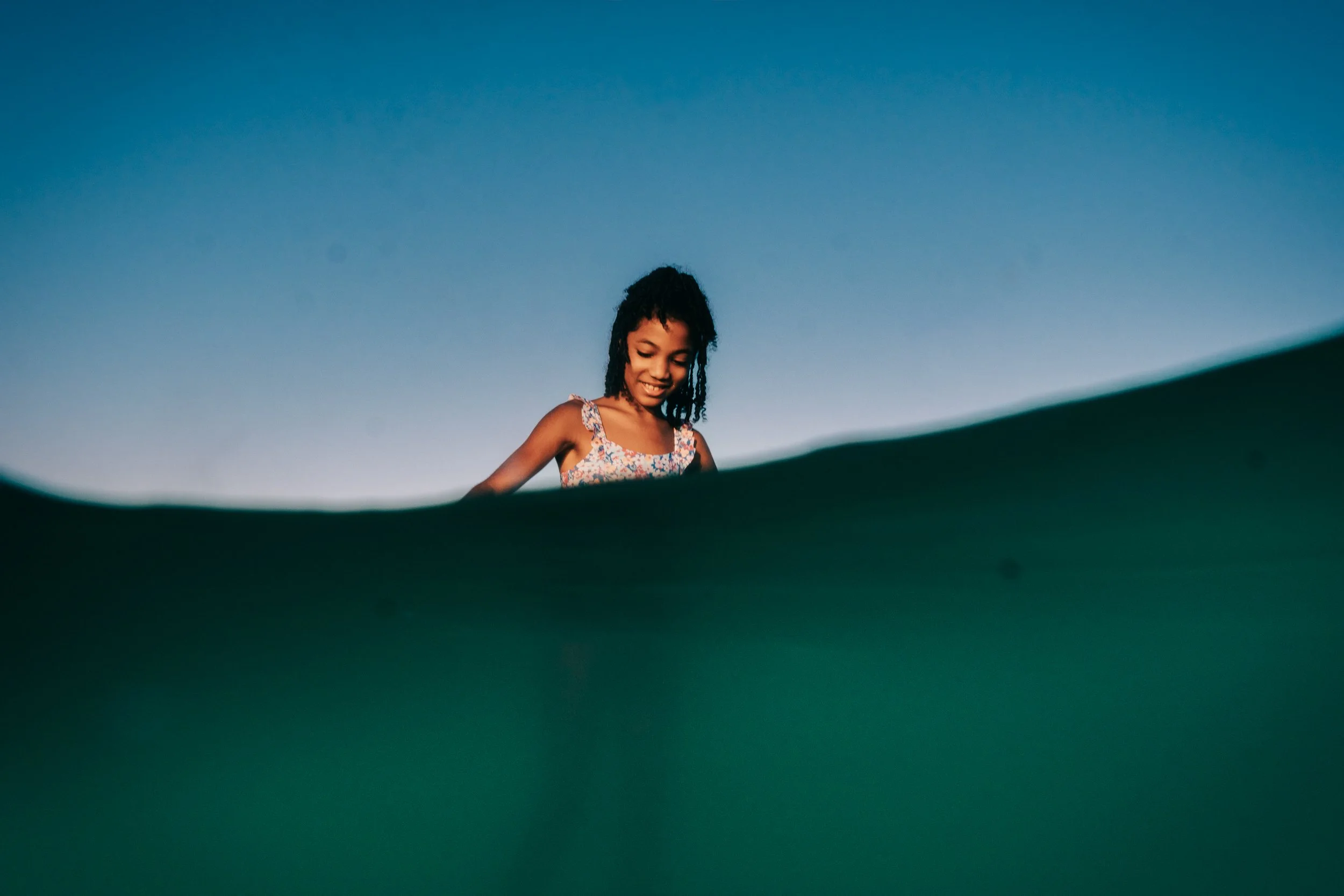 Young girl smiling and looking down, seen from below against a clear blue sky.