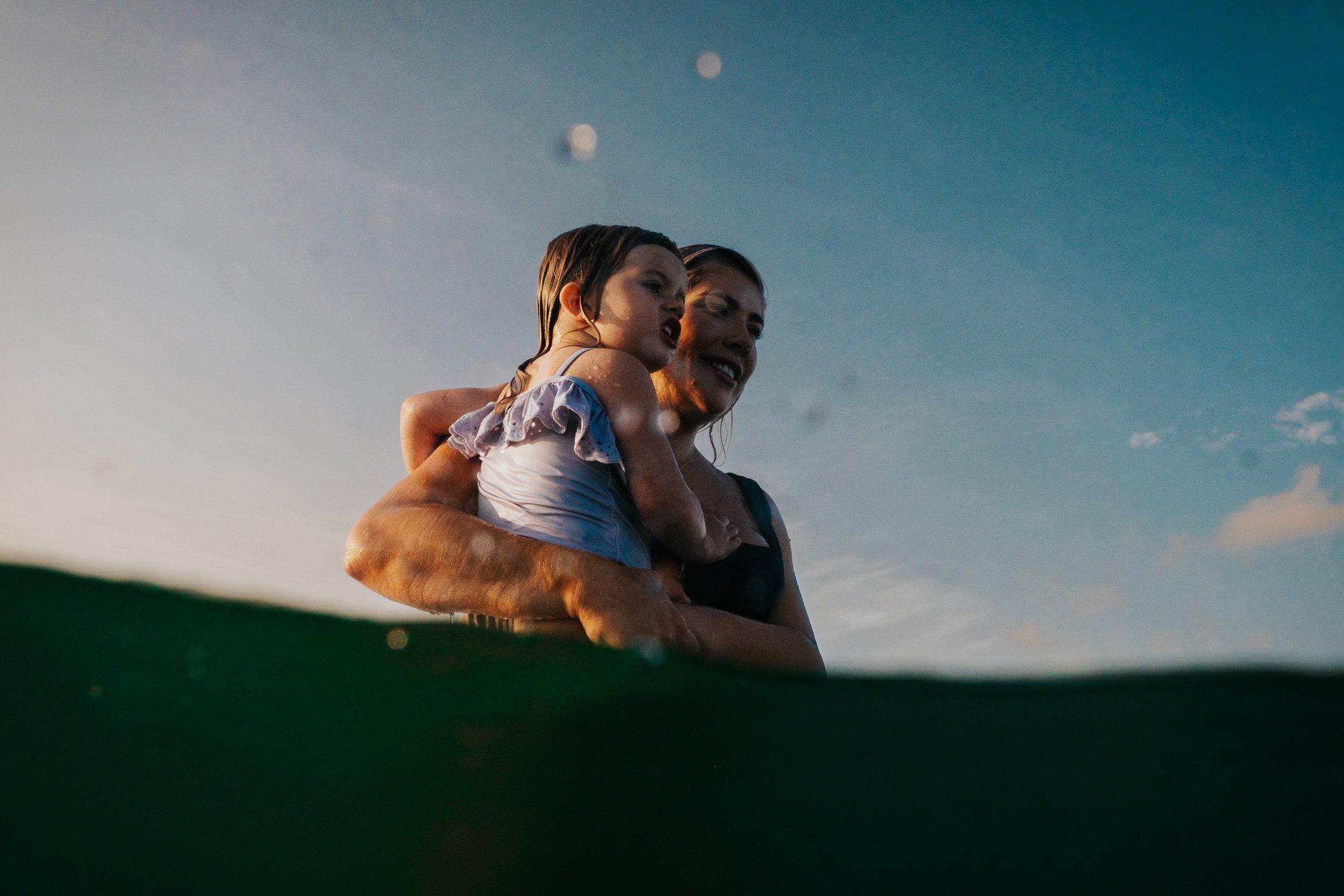 A woman holding a young girl in her arms, both wet, with the sky and the moon visible in the background.
