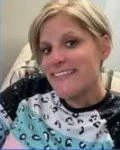 A woman with blonde hair smiling, wearing a patterned hospital gown, in a hospital setting.