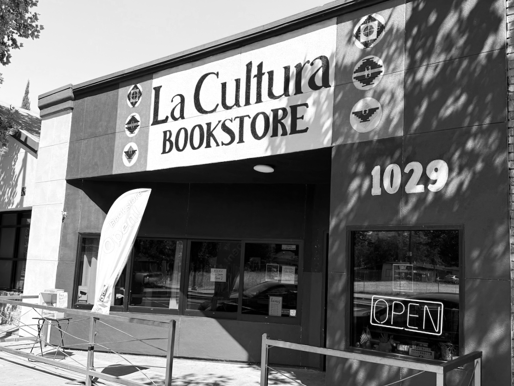 Black and white photo of La Cultura bookstore storefront with an open sign, building number 1029, and a flag with the store's name.