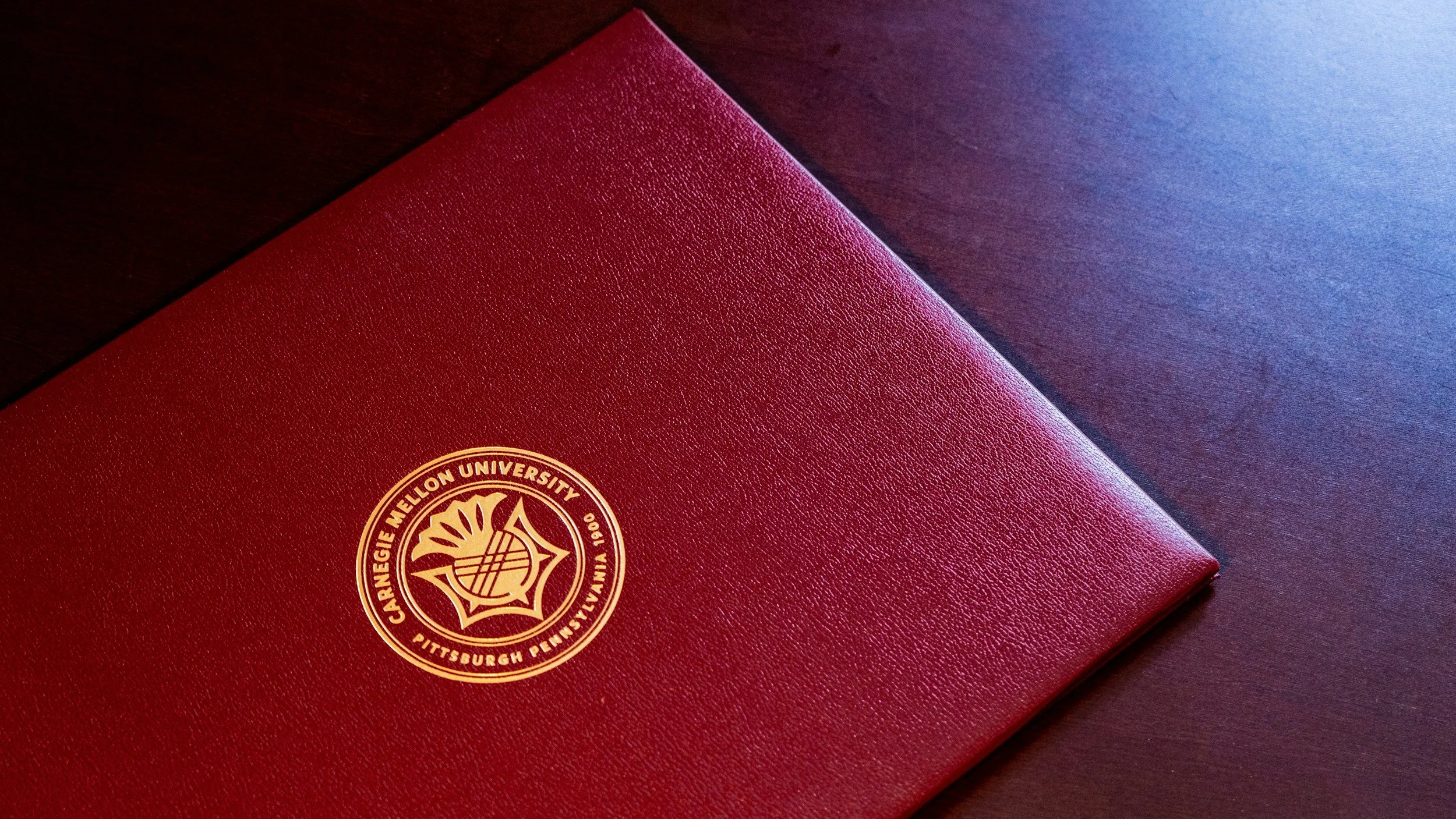 Red leather folder with the Carnegie Mellon University crest on the cover, placed on a dark wooden surface.