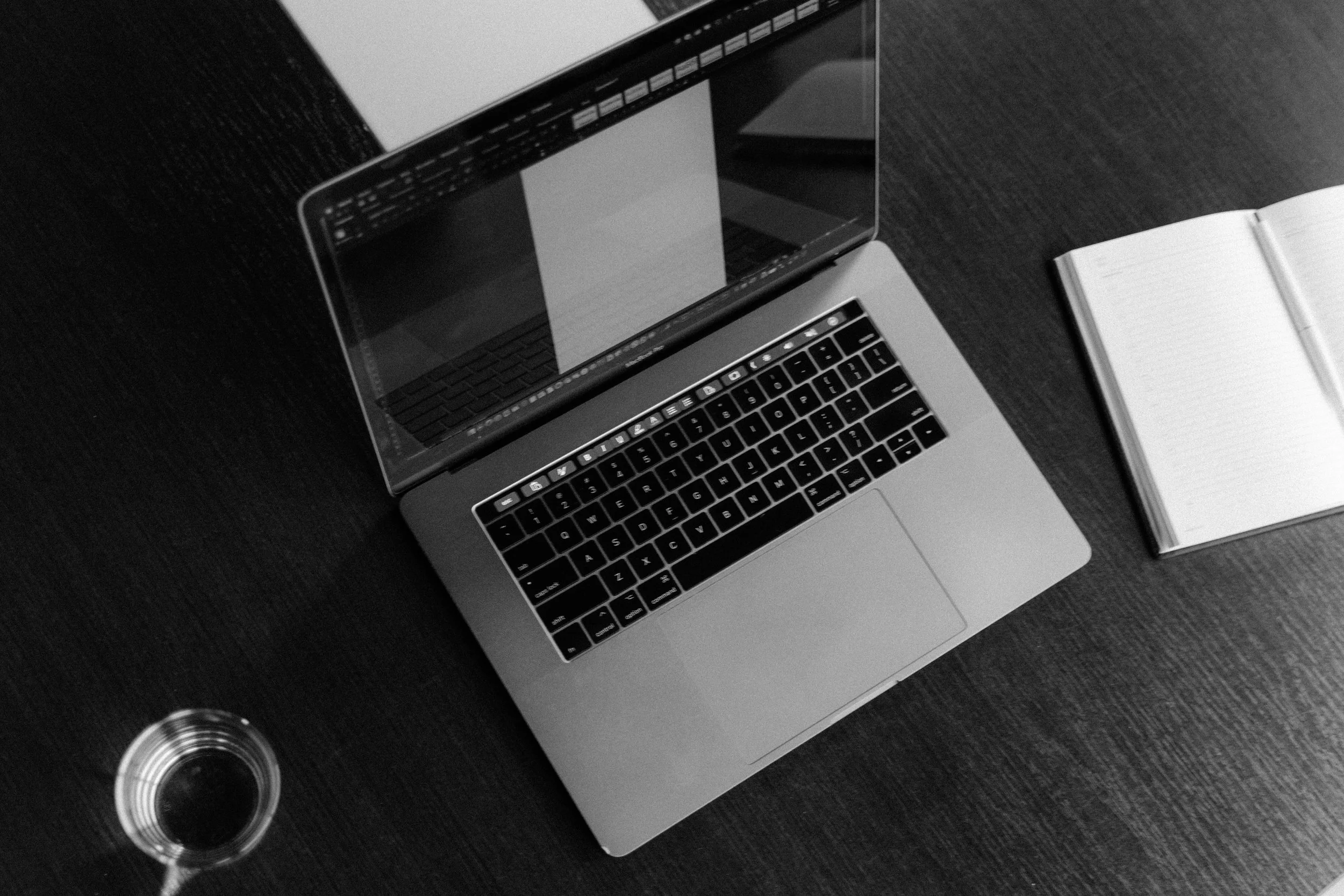 A laptop computer, two open cans of soda, and an open notebook with a pen on a dark wooden table.