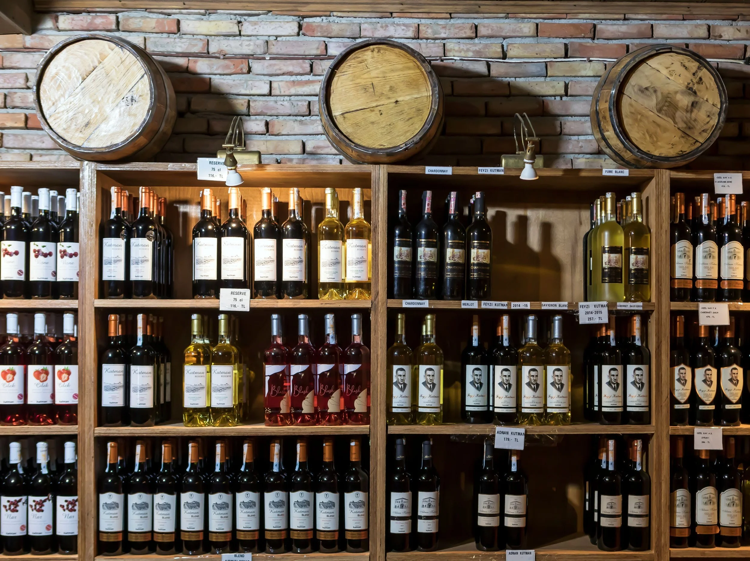 Wooden barrels mounted on a brick wall above shelves of wine bottles in a store.