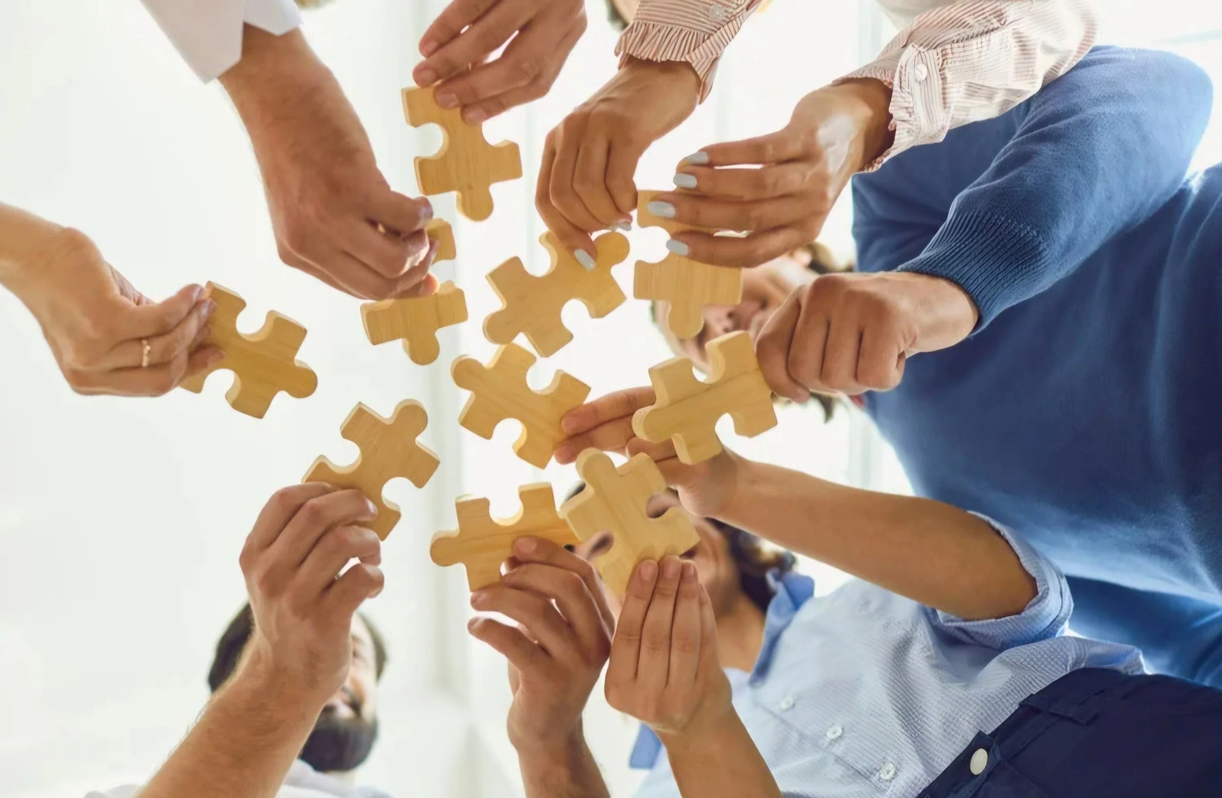 Multiple hands of diverse people connecting wooden puzzle pieces together.