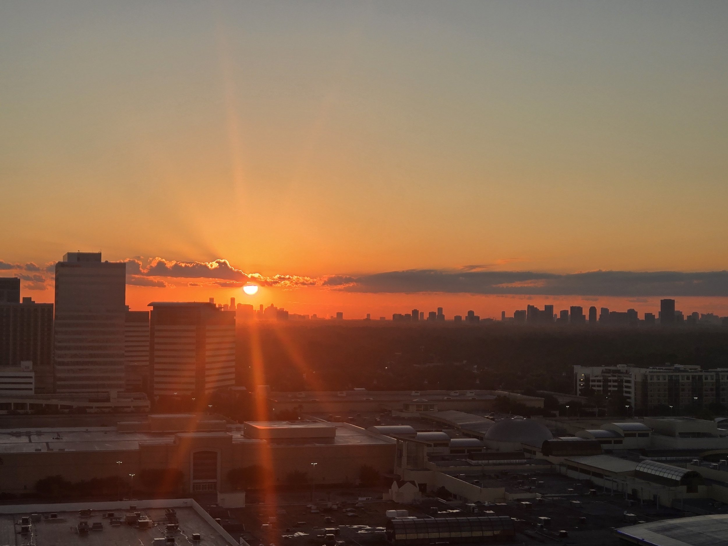 Sunset over a city skyline with high-rise buildings and clouds, vibrant orange and red hues in the sky.