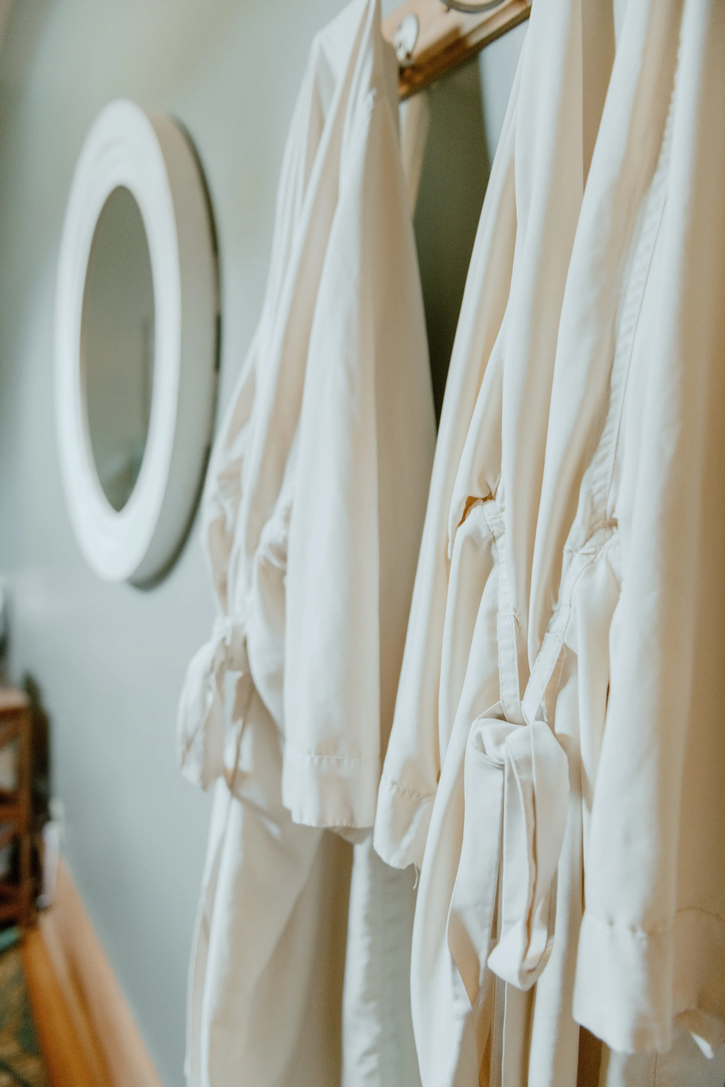 Cream-colored robes hanging on a wooden rack, with a mirror reflecting the room.